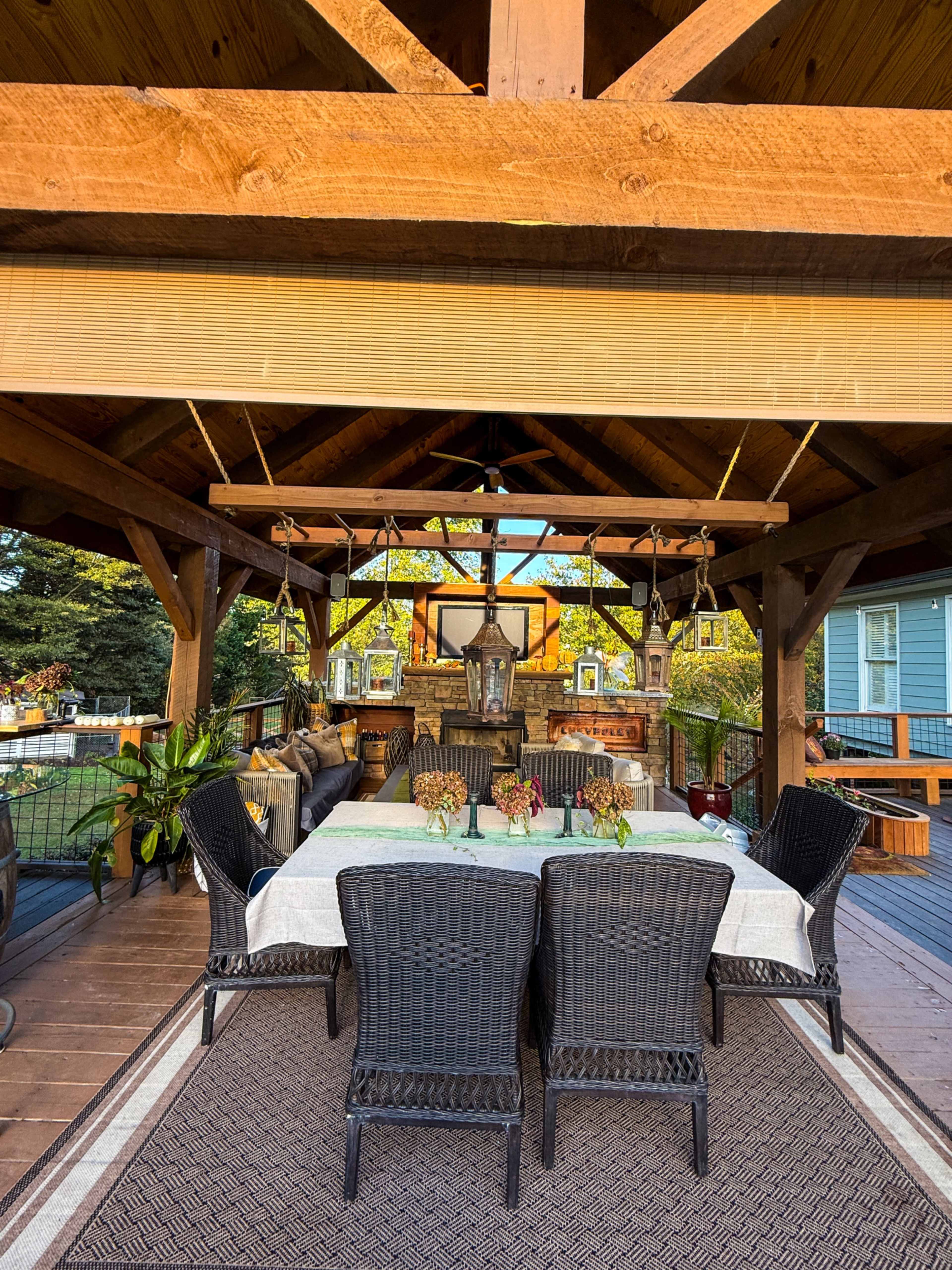 The image shows a covered outdoor dining area with a table set for meals, surrounded by wicker chairs and decorative plants.
