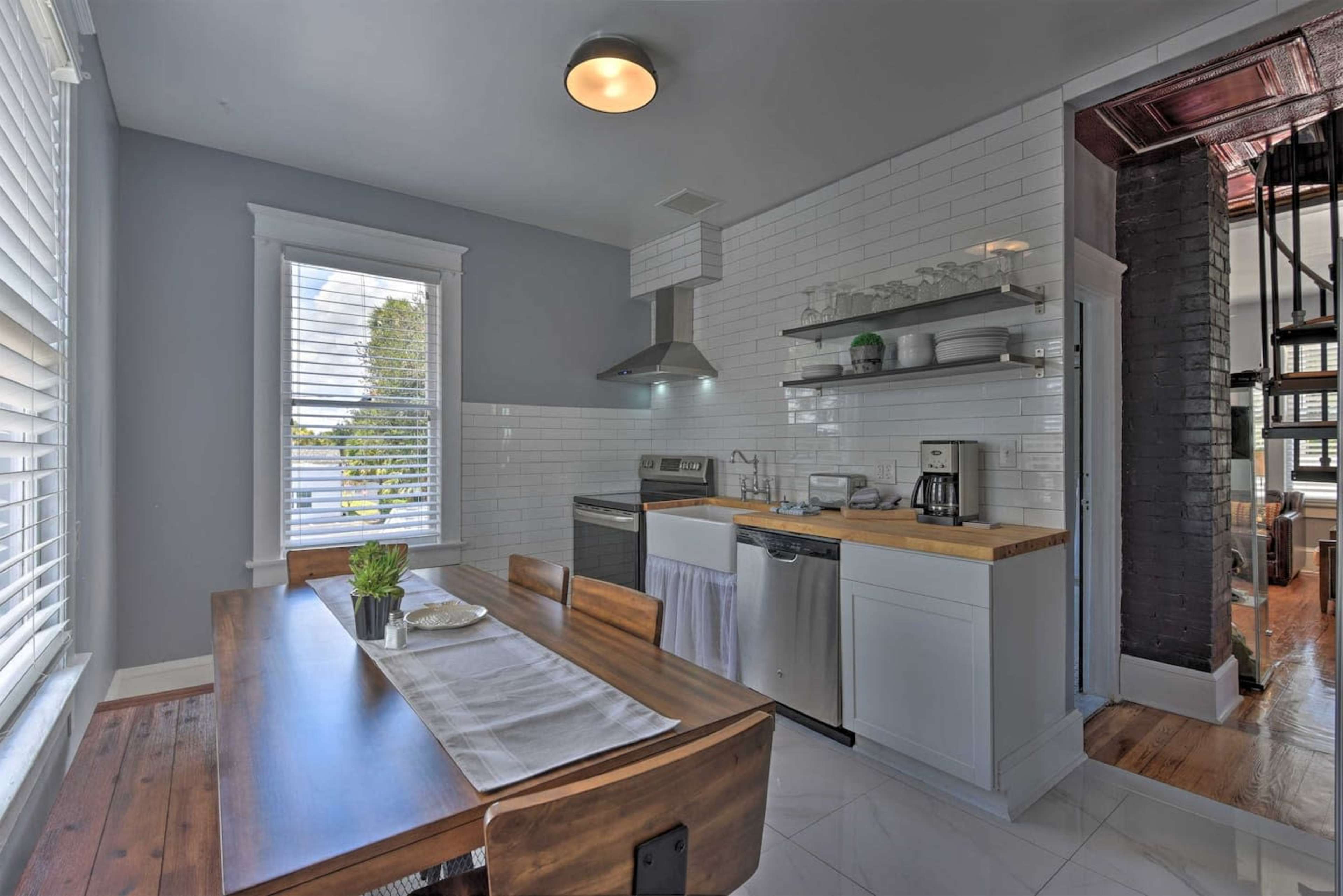A modern kitchen with white tile walls, a wooden dining table, stainless steel appliances, and a minimalistic design.