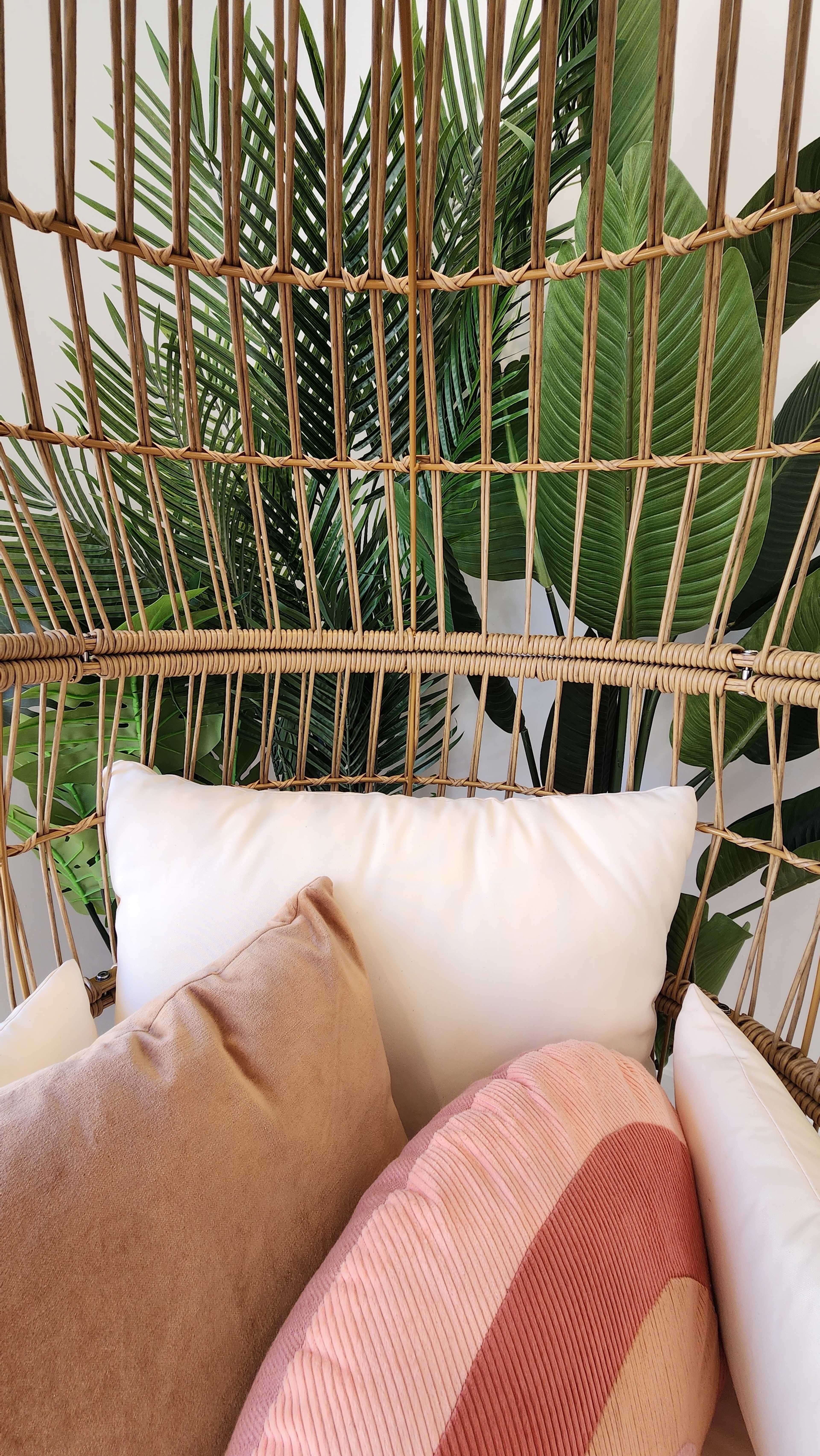 The image shows a cozy seating nook with plush pillows surrounded by large green leaves in a woven, open-frame structure.