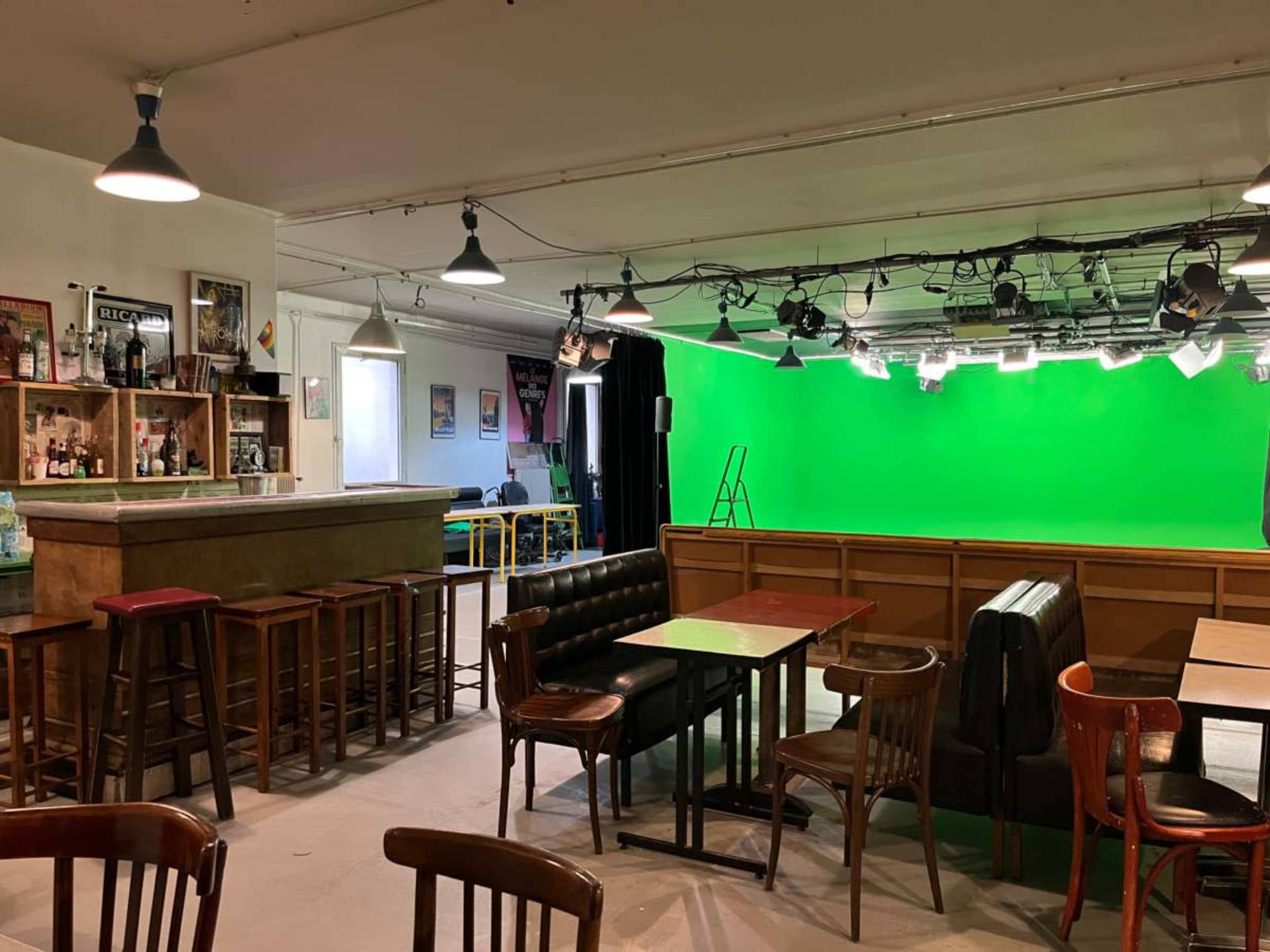 The image shows a spacious bar area with wooden seating and a green screen backdrop, indicating a studio or event space.