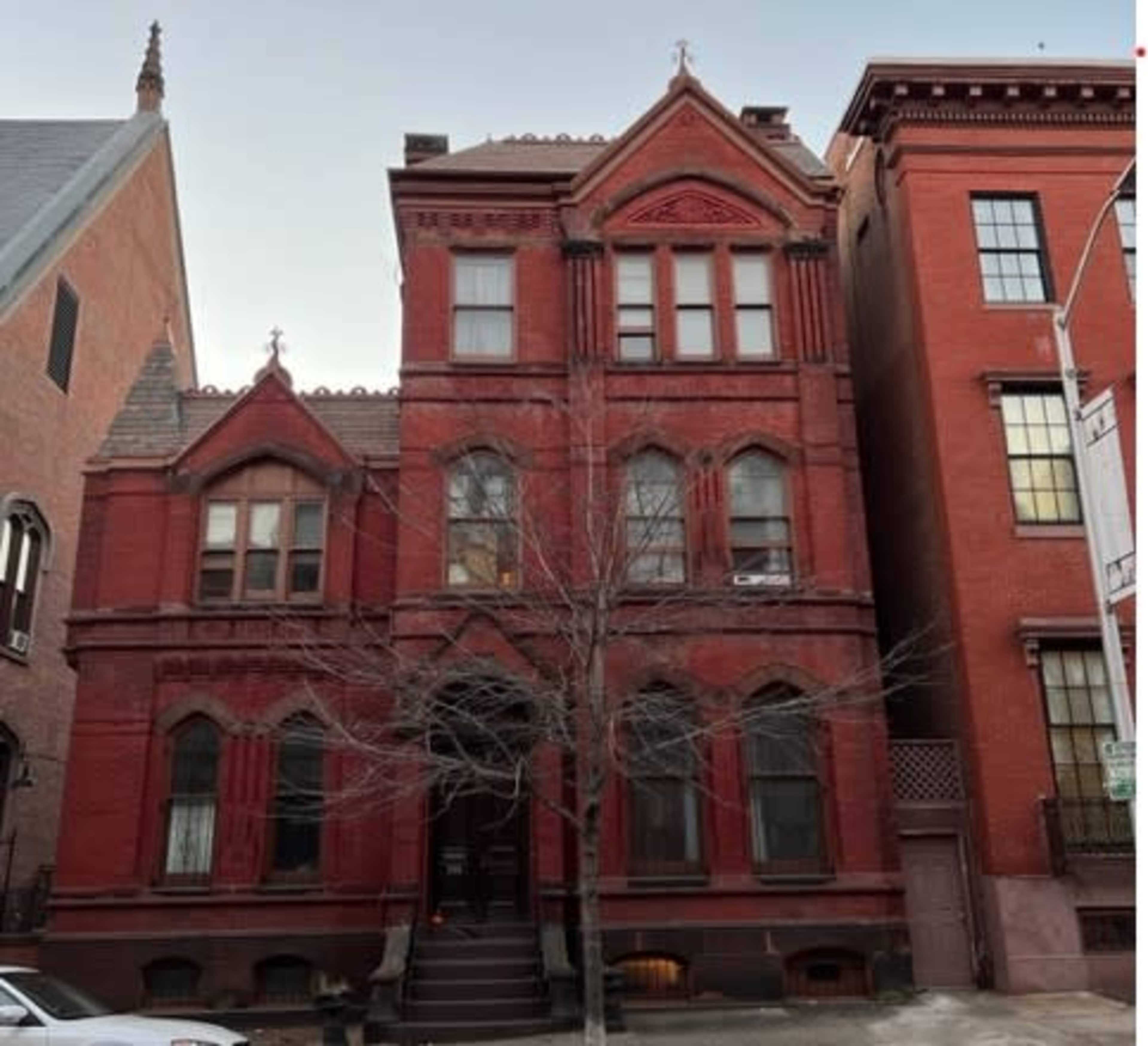 A three-story red brick Victorian-style house with decorative elements, flanked by two taller brick buildings.