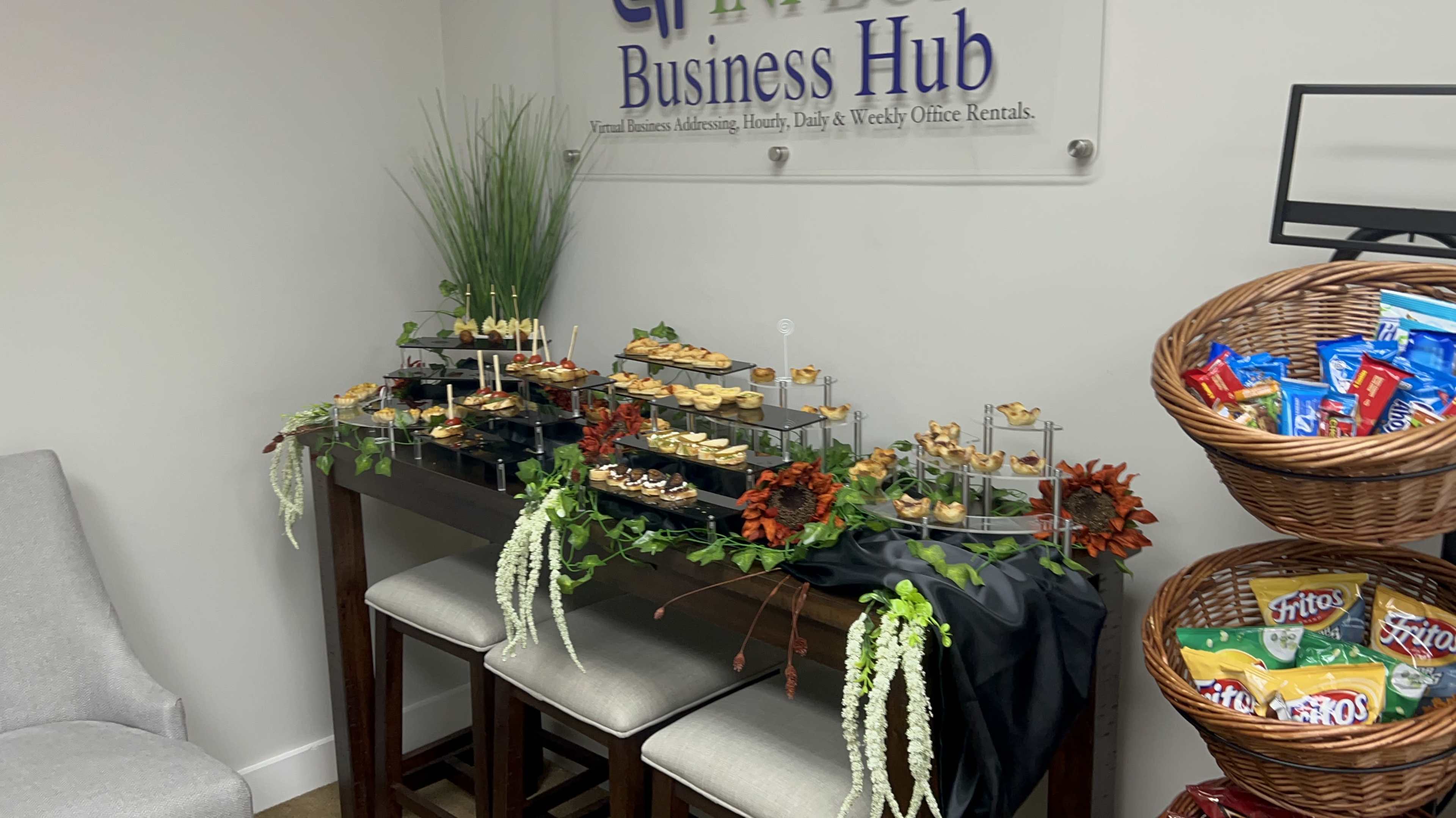A buffet table with assorted appetizers and snacks is set up against a wall displaying a sign for "Business Hub."