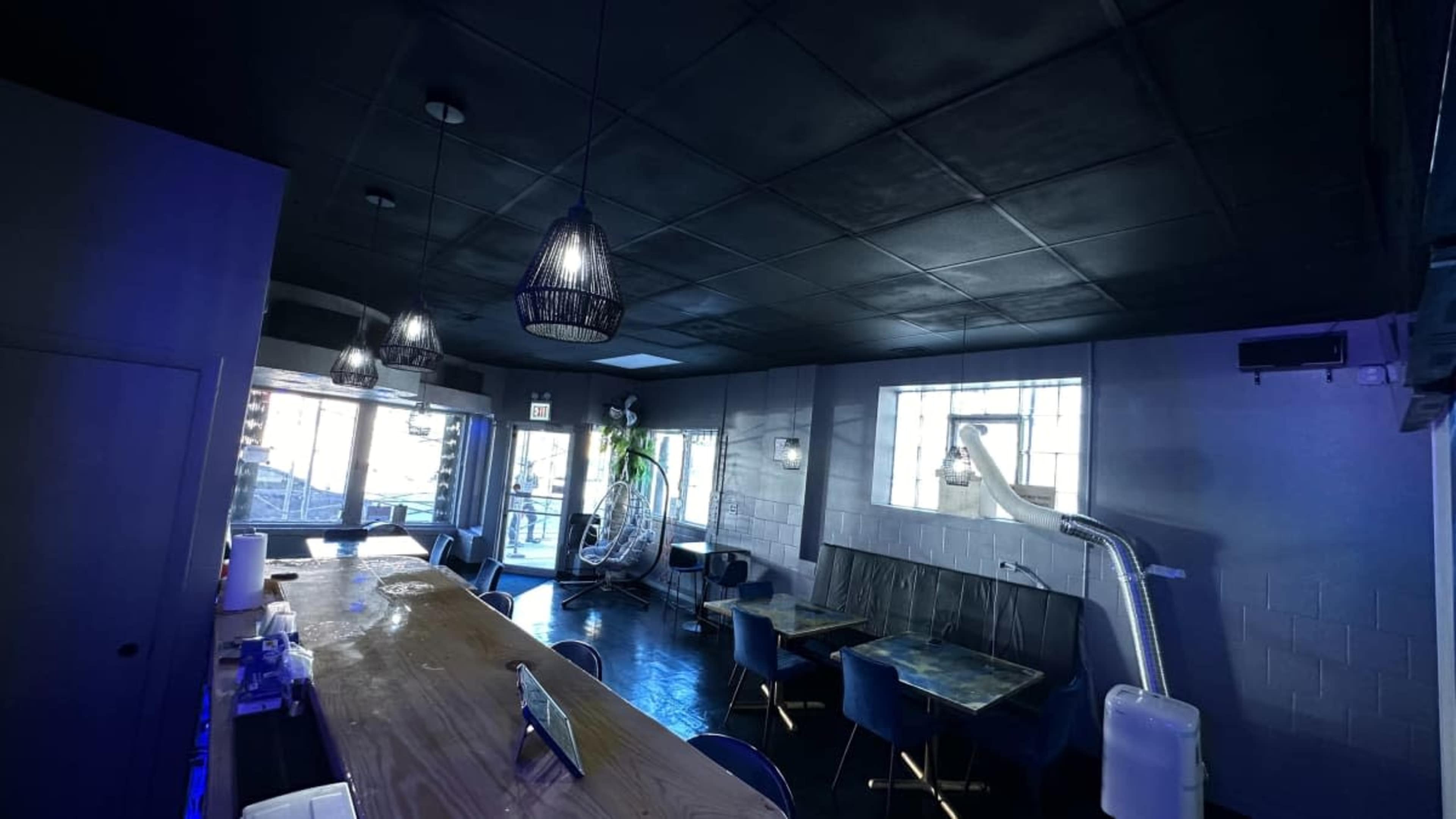 The image shows the interior of a modern café with a wooden counter, blue upholstered chairs, and large windows allowing natural light to enter.