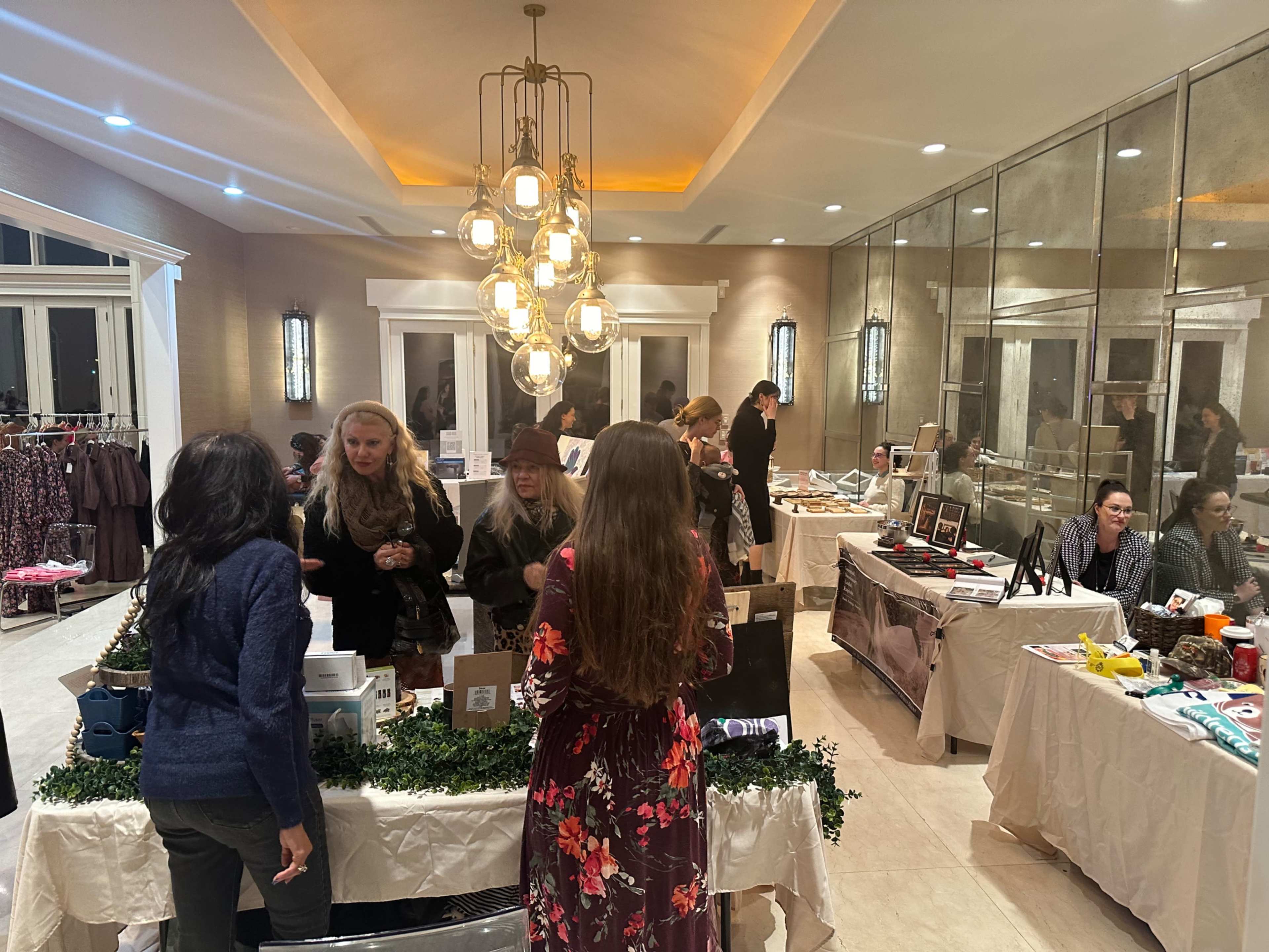 A group of women engage with various vendors at a well-lit social event featuring several tables with displayed items.