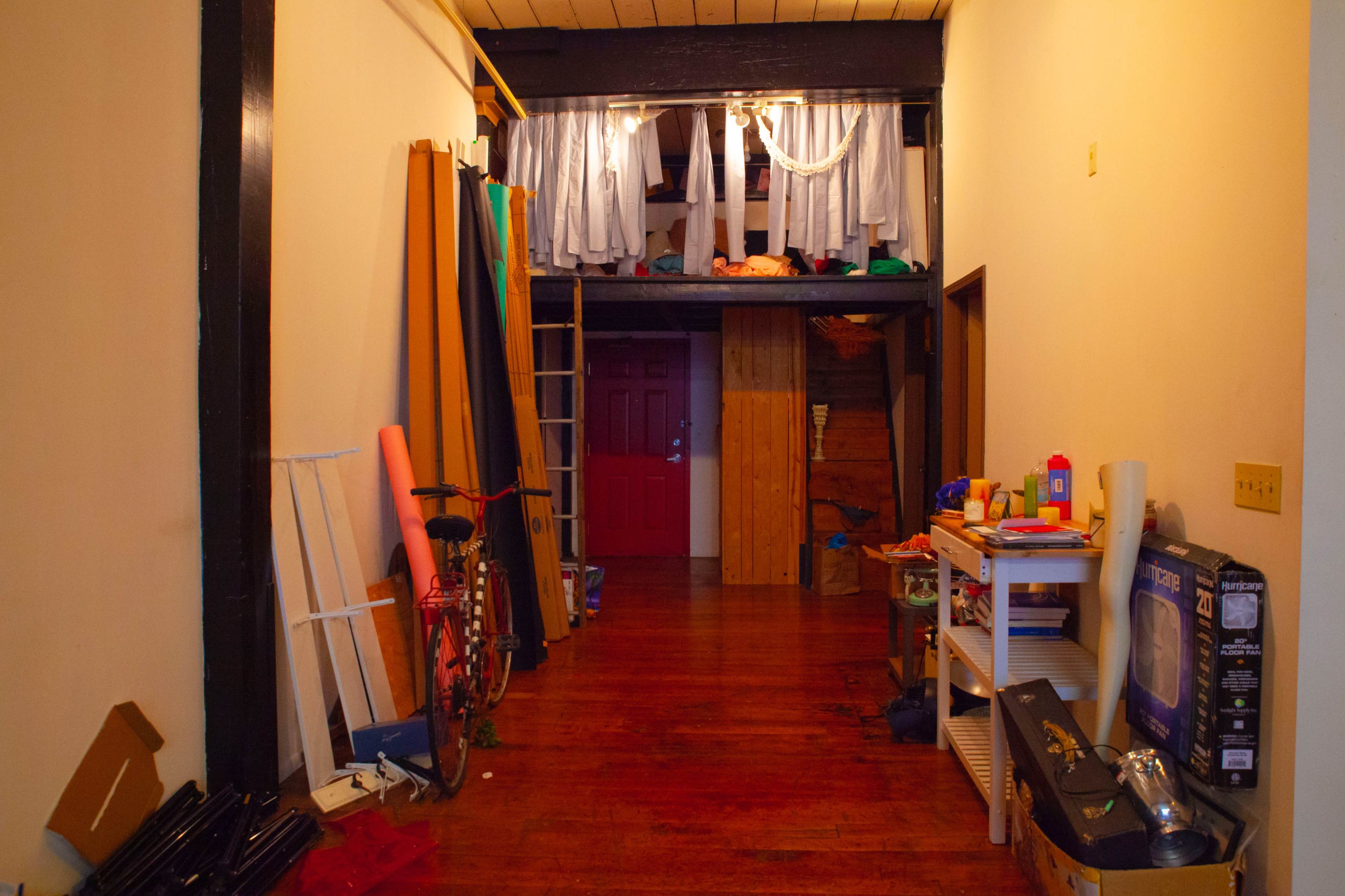 A long hallway is lined with various items, including a bicycle and stacks of materials, leading to a door at the far end.