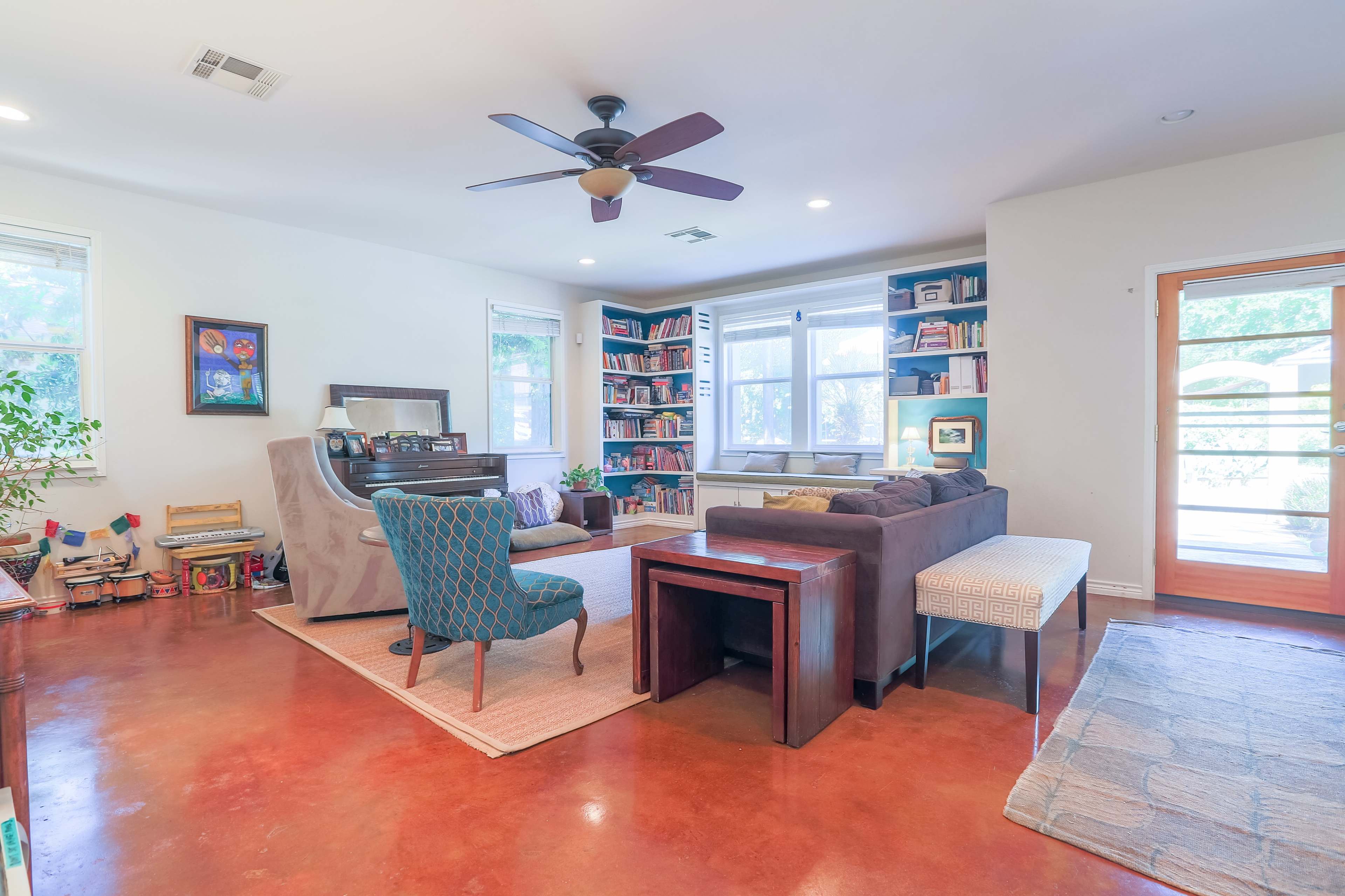 The living room features a piano, bookshelves filled with books, and a mix of modern and traditional furniture arranged around a central rug.