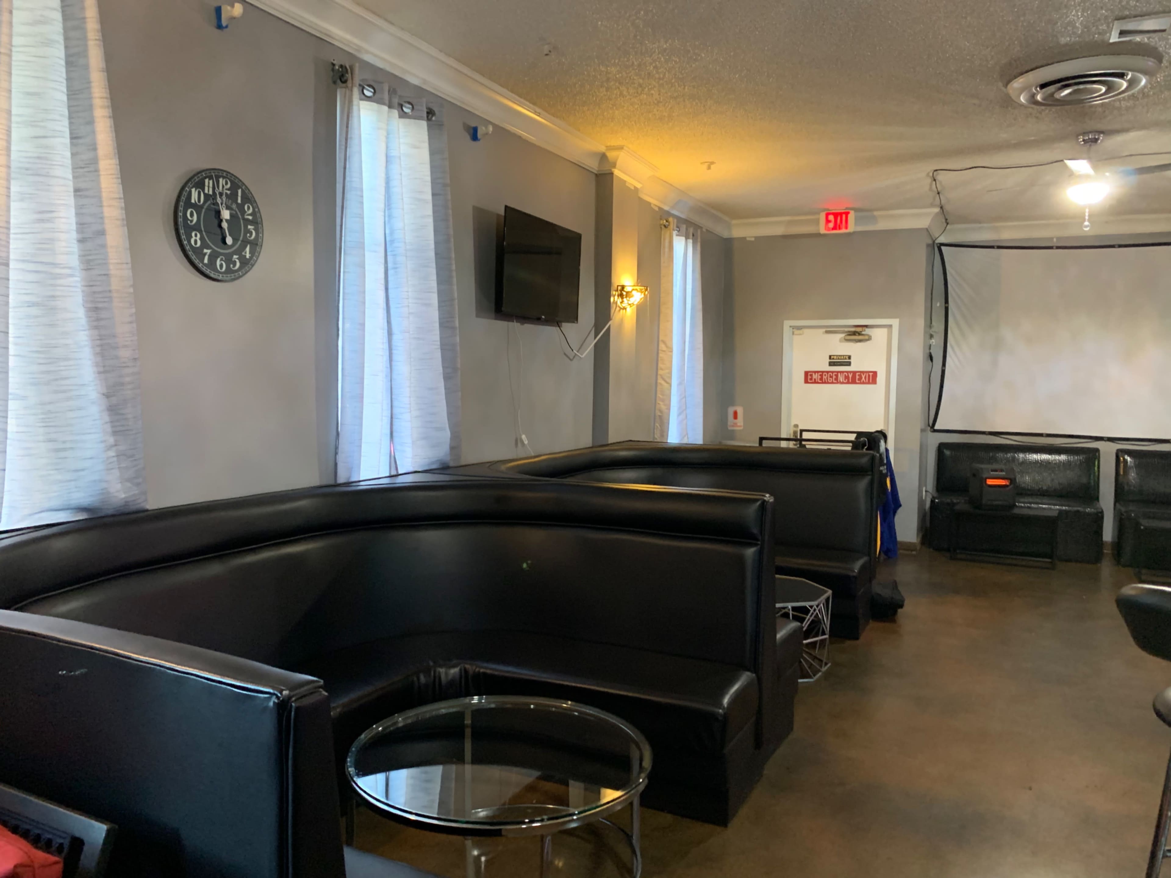A lounge area with black leather seating, a round glass table, and a wall-mounted television.