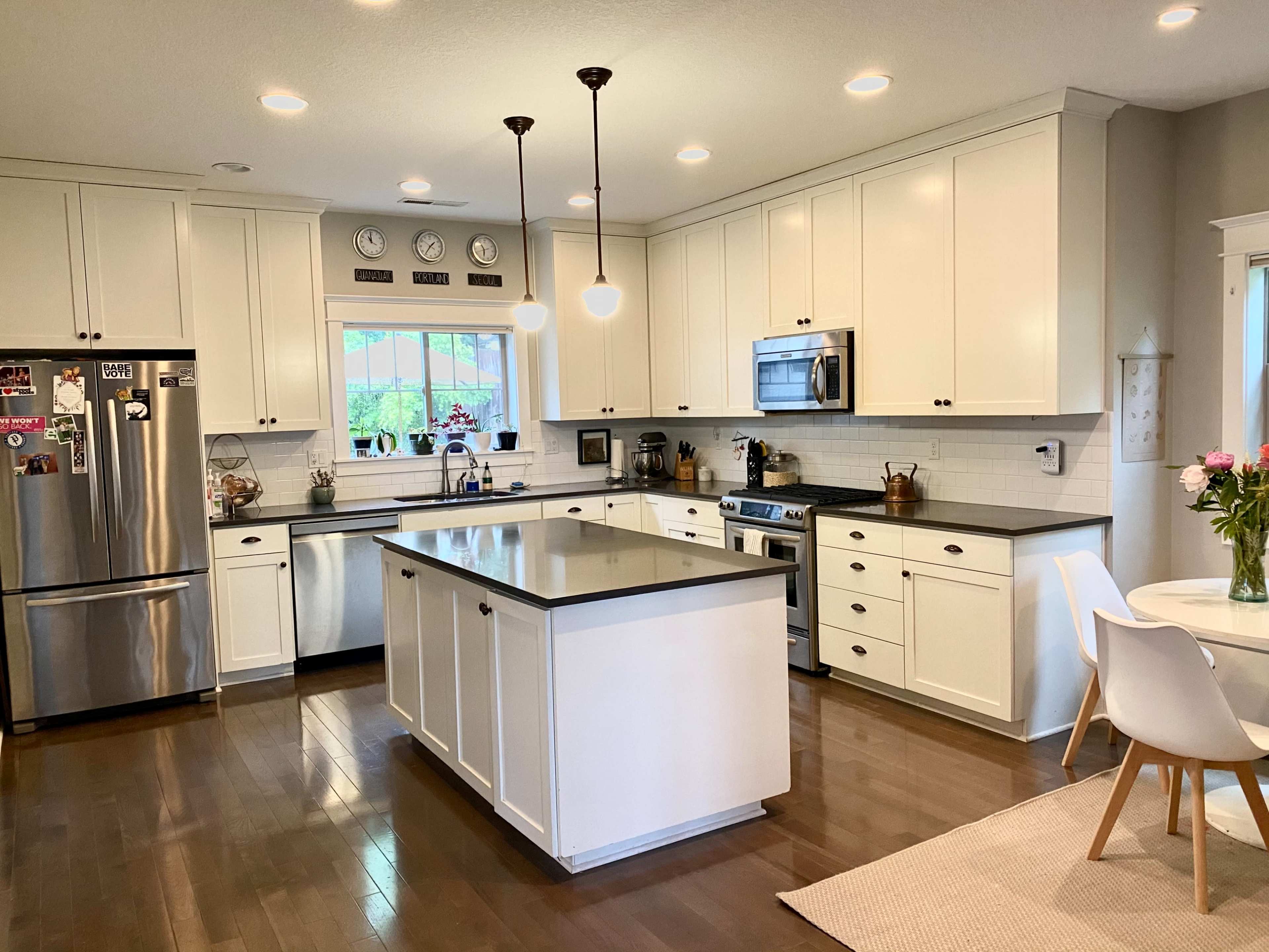 A modern kitchen with white cabinets, stainless steel appliances, and a central island with seating, alongside a small dining area.