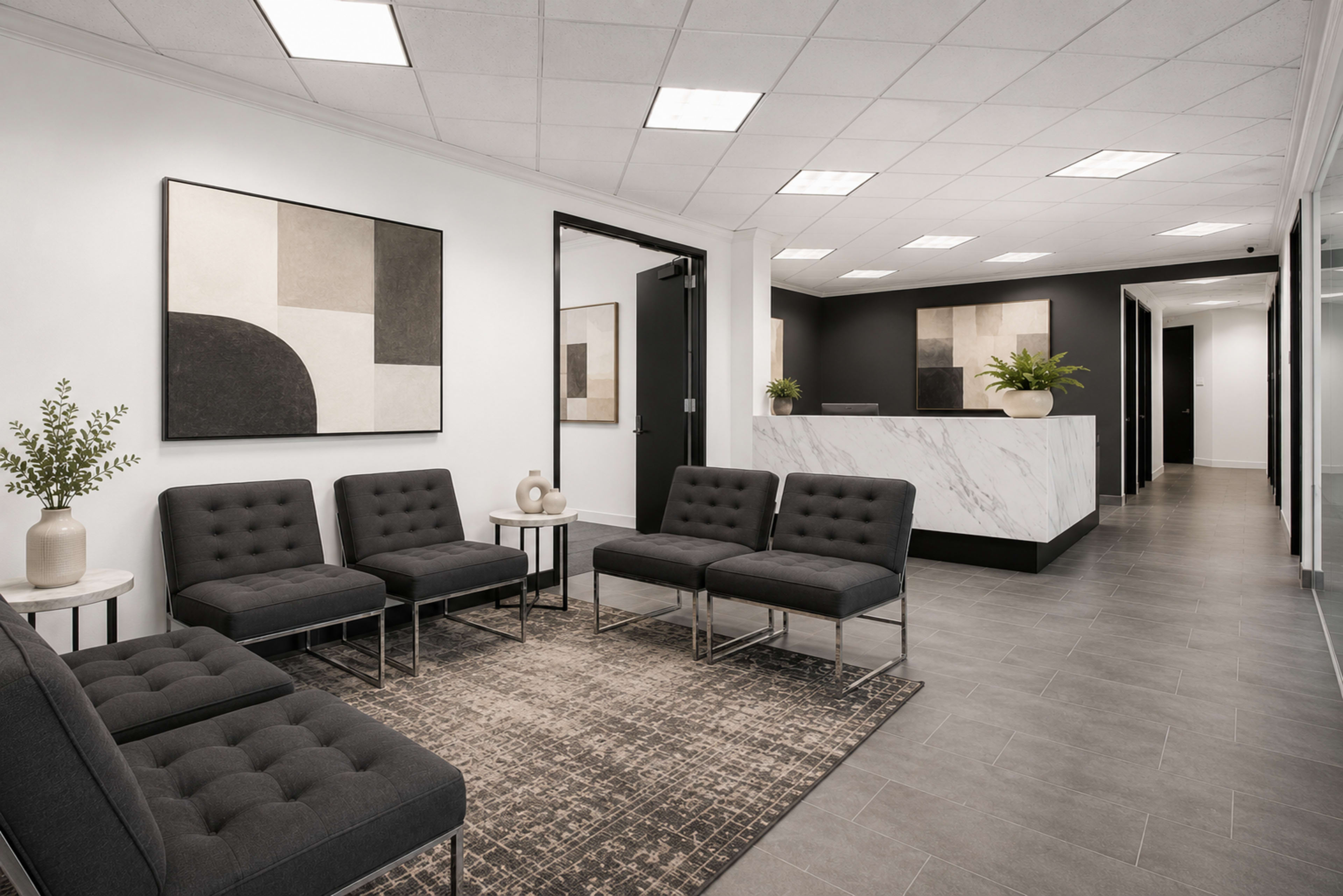 The image shows a modern reception area with gray seating, a patterned rug, and a marble front desk in a well-lit space.