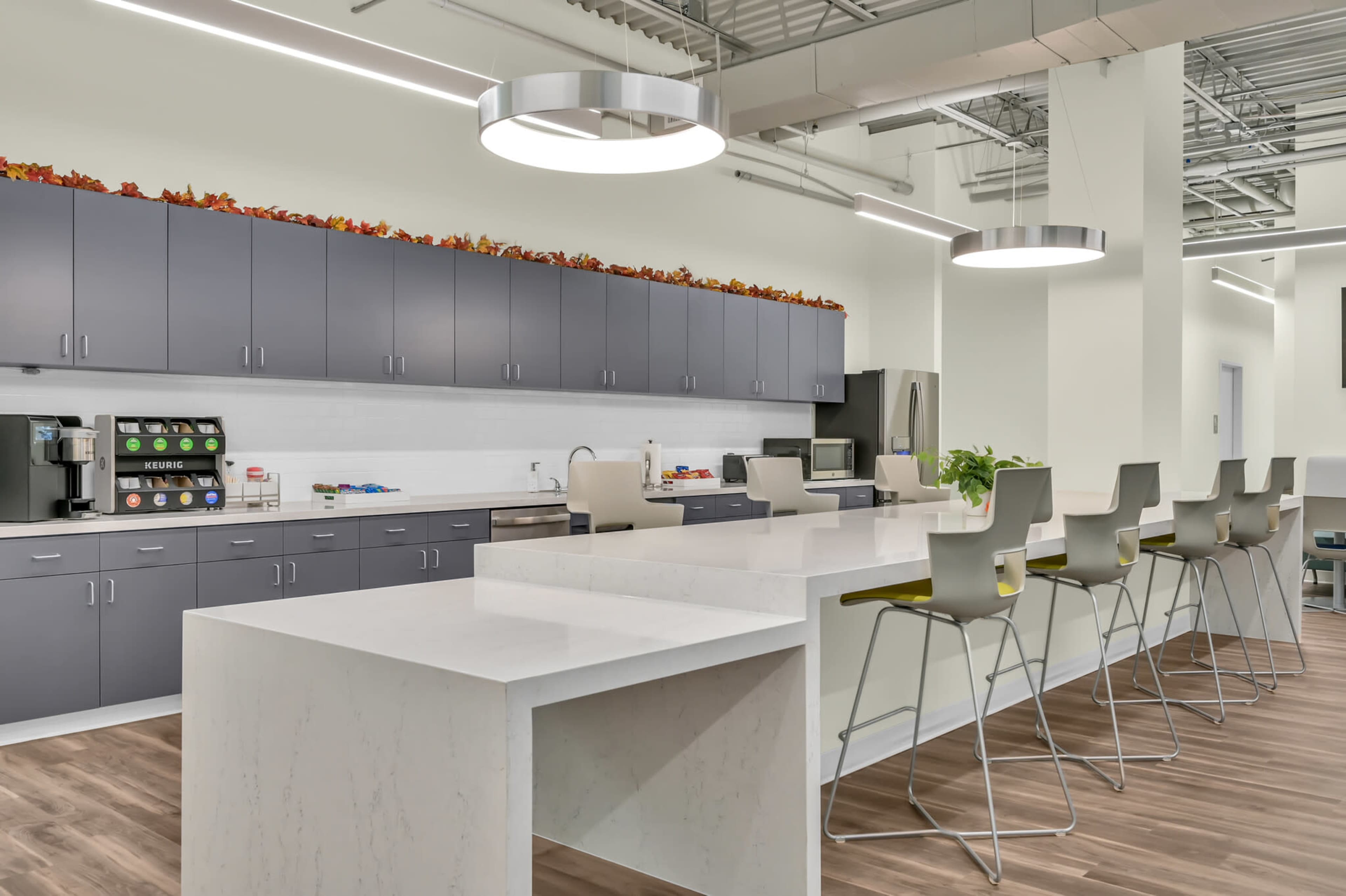 The image shows a modern kitchen area with gray cabinets, a white countertop, and barstools, illuminated by circular pendant lights.