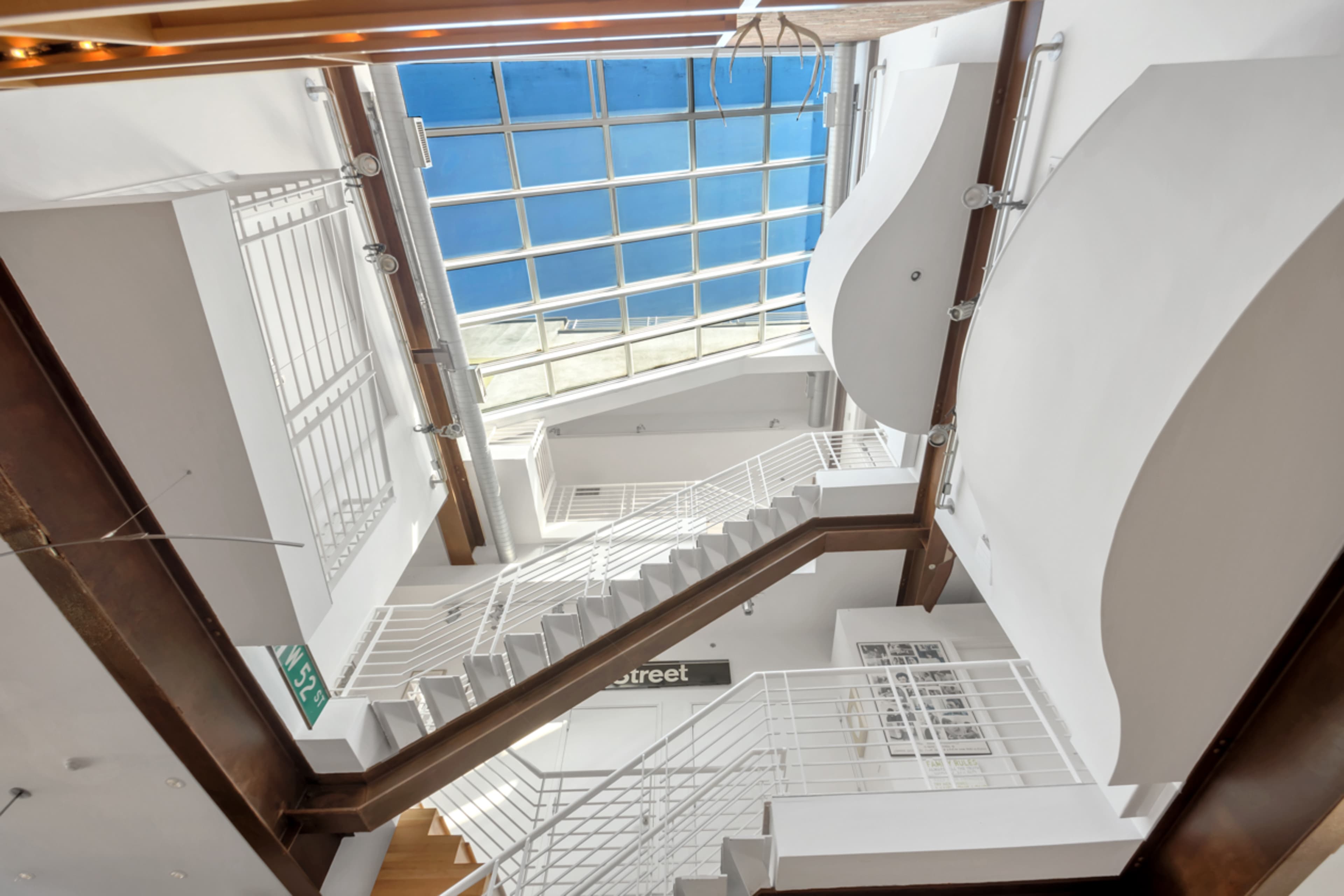 The image shows a modern interior featuring a staircase with a glass roof above and white walls.