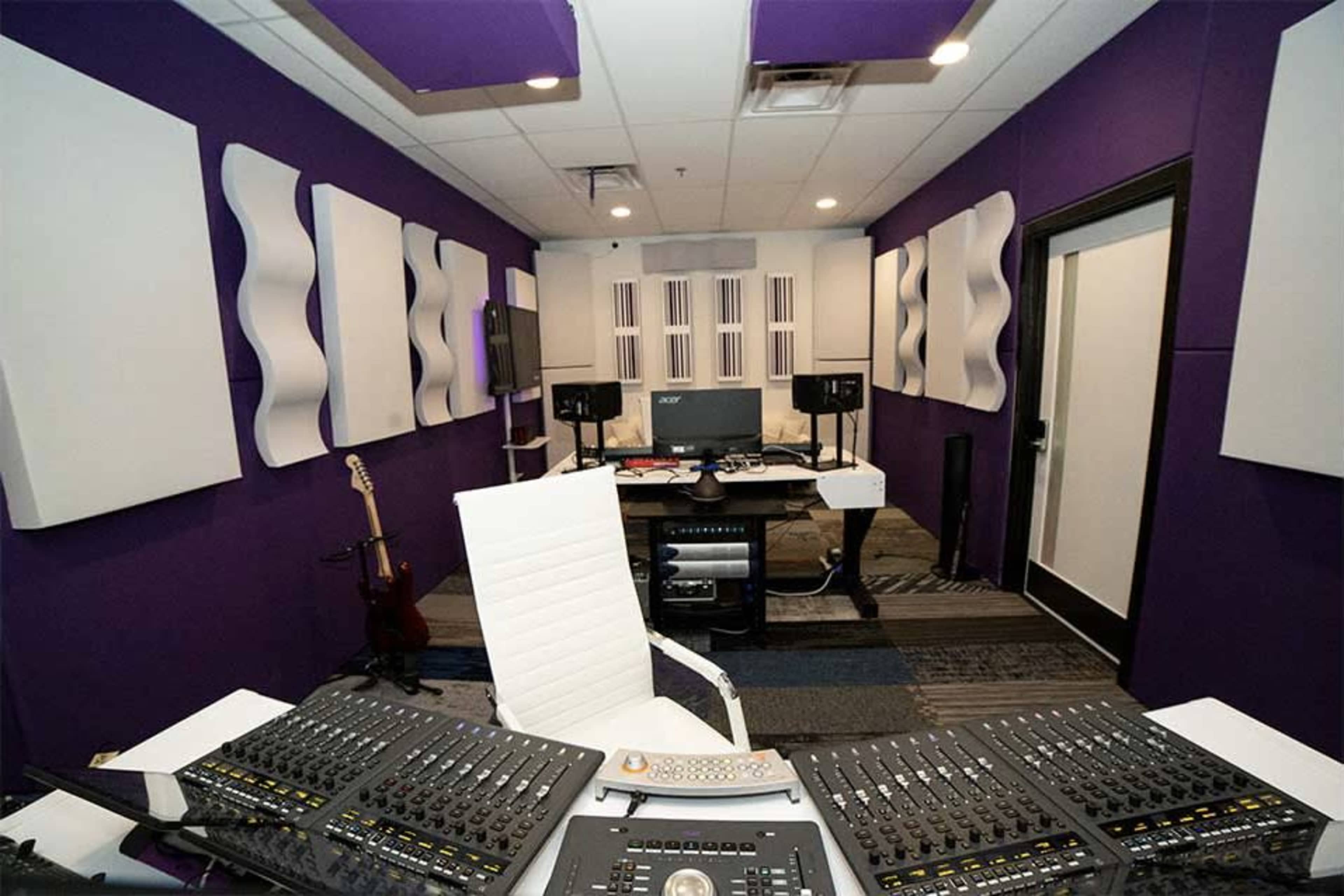A modern recording studio with a mixing console, computer setup, and soundproofed walls.