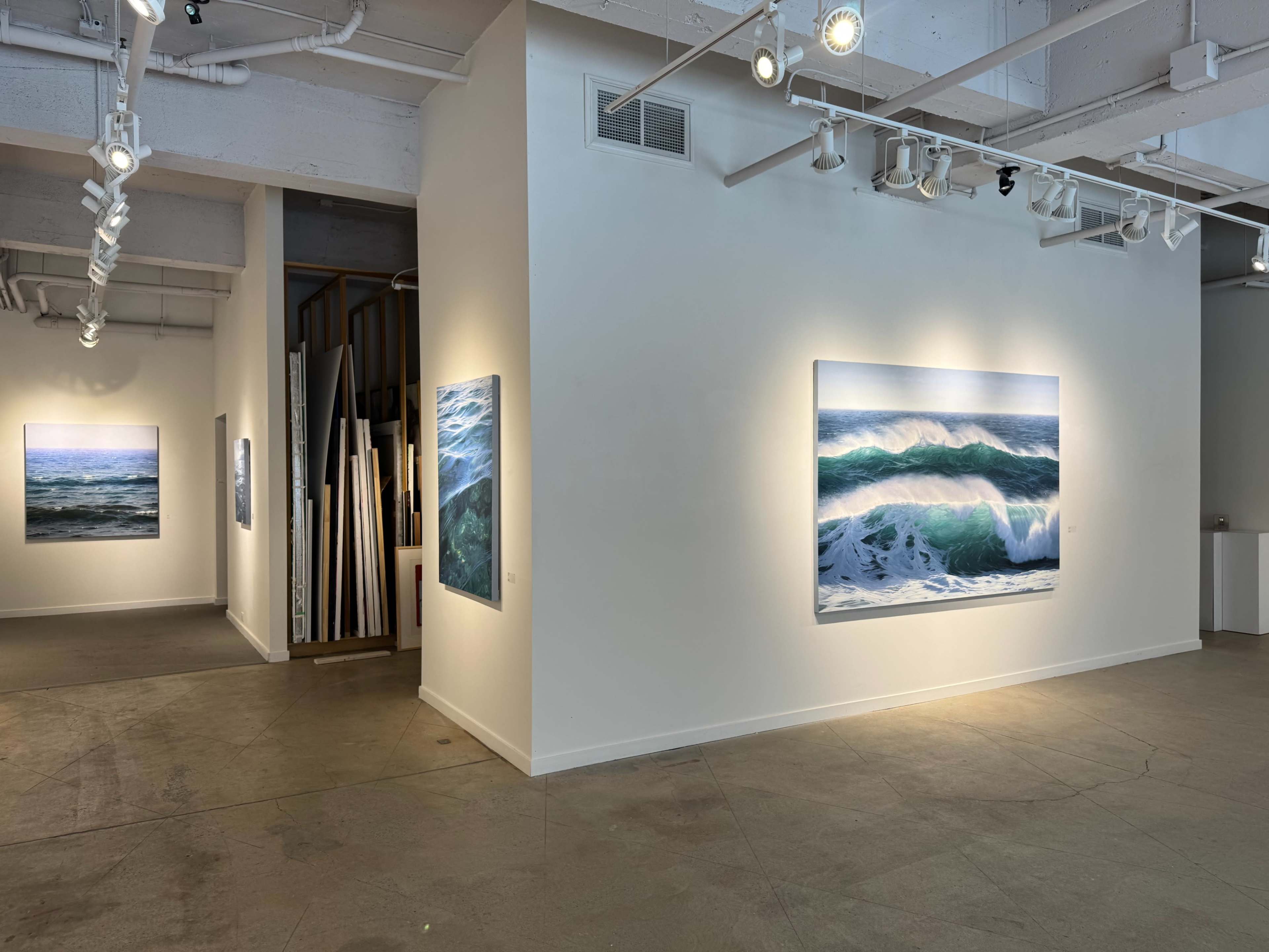 The image shows an art gallery with large seascape paintings on the white walls, and additional artwork visible in the background.