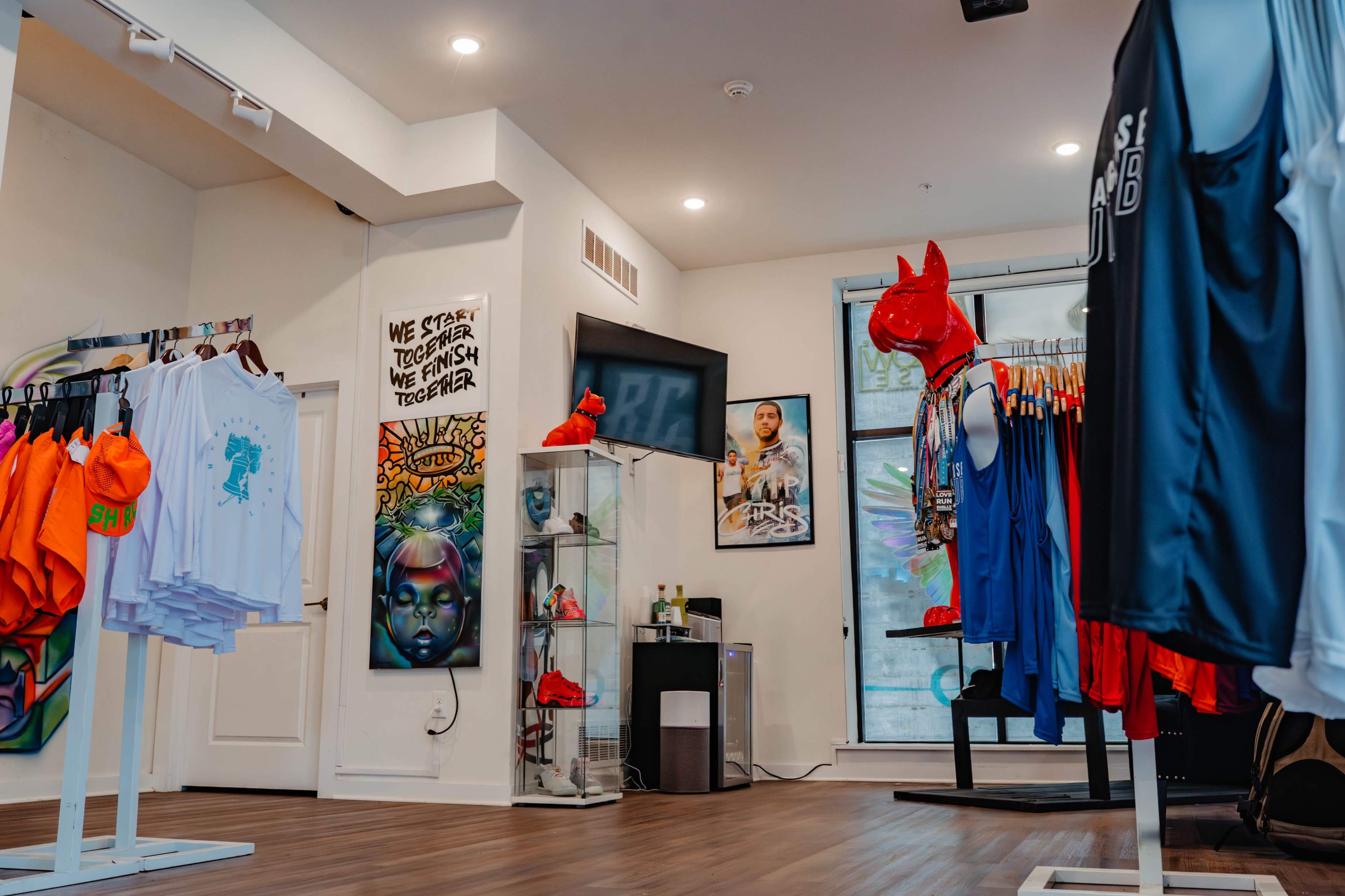 A retail store interior with apparel on display, including colorful shirts and a red mannequin, along with artwork and a television on the walls.