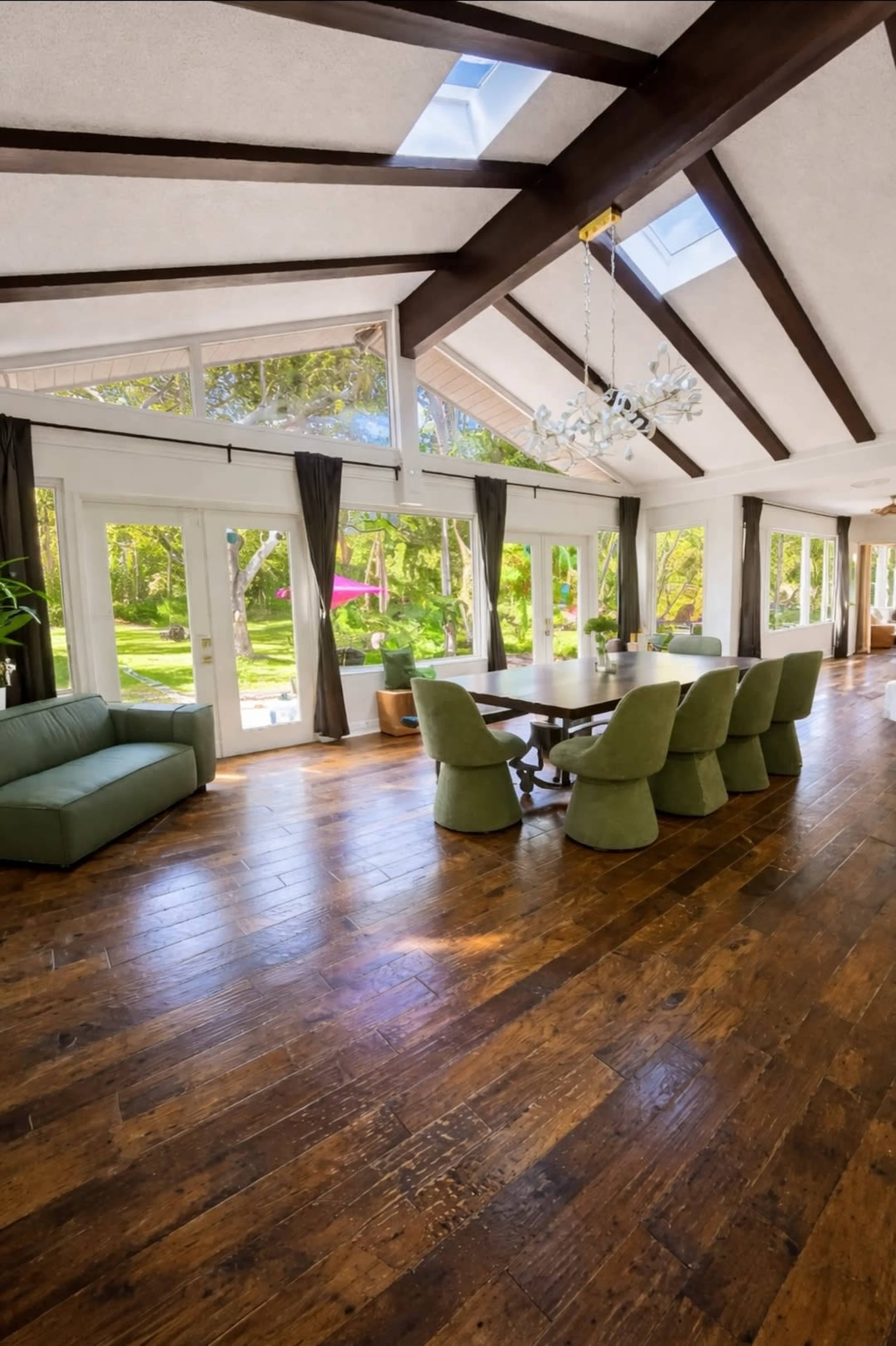 The image depicts a spacious dining area with a wooden floor, large windows, and a table surrounded by upholstered chairs.
