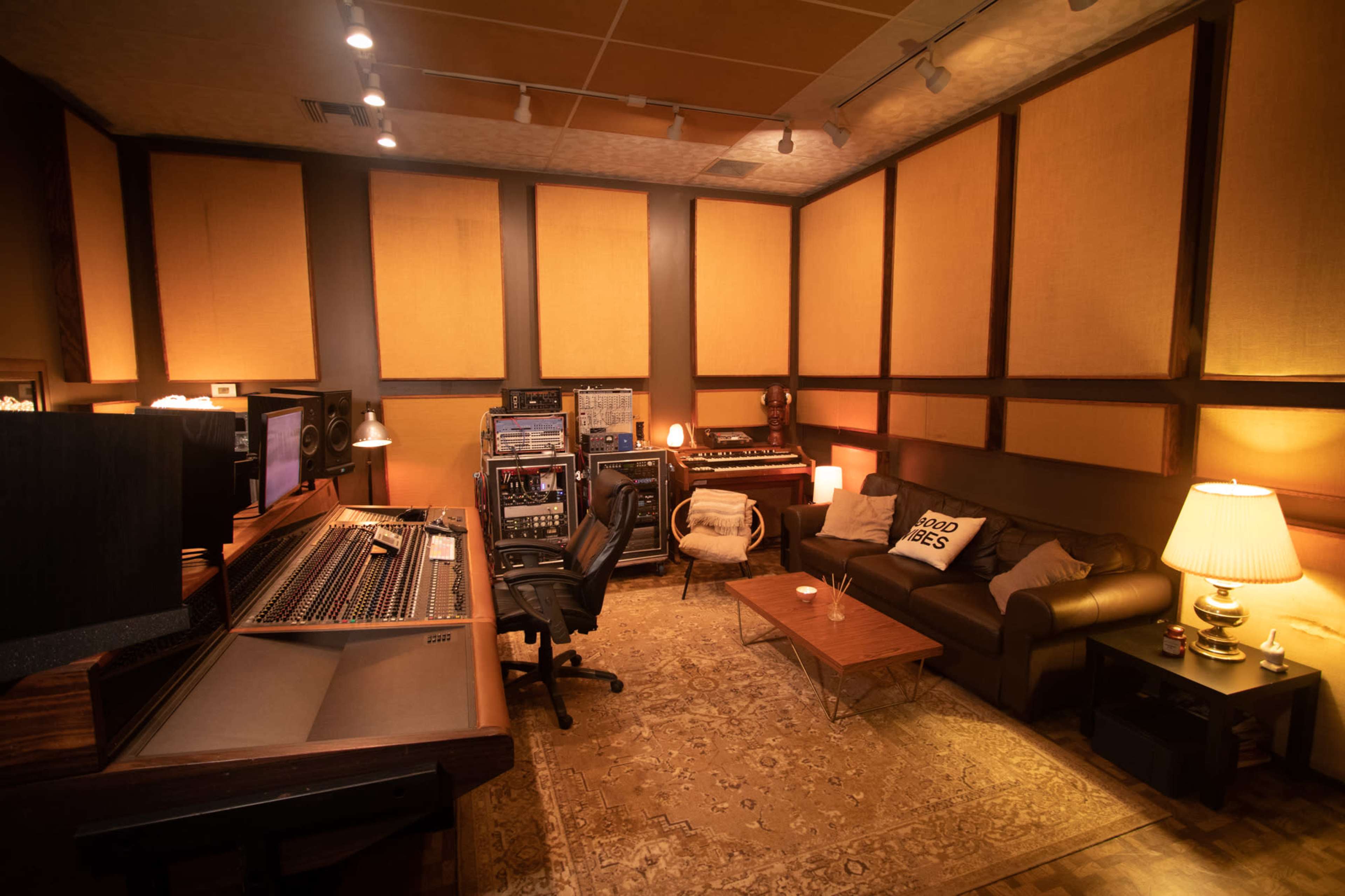 A recording studio with a mixing console, audio equipment, a couch, and warm lighting.