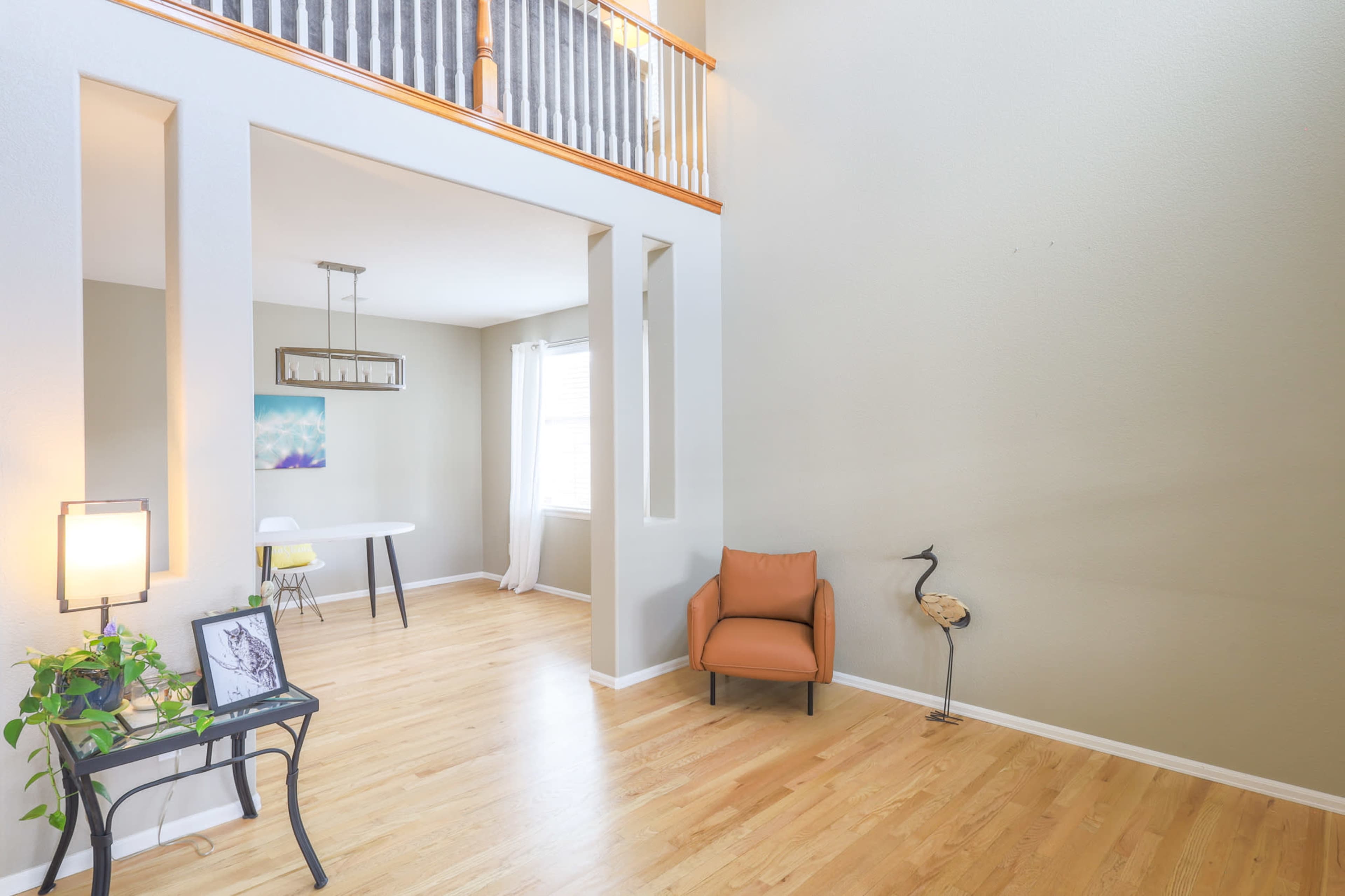 A spacious interior room featuring wooden flooring, a light-colored wall, a brown chair, a small table with chairs, and a decorative plant.