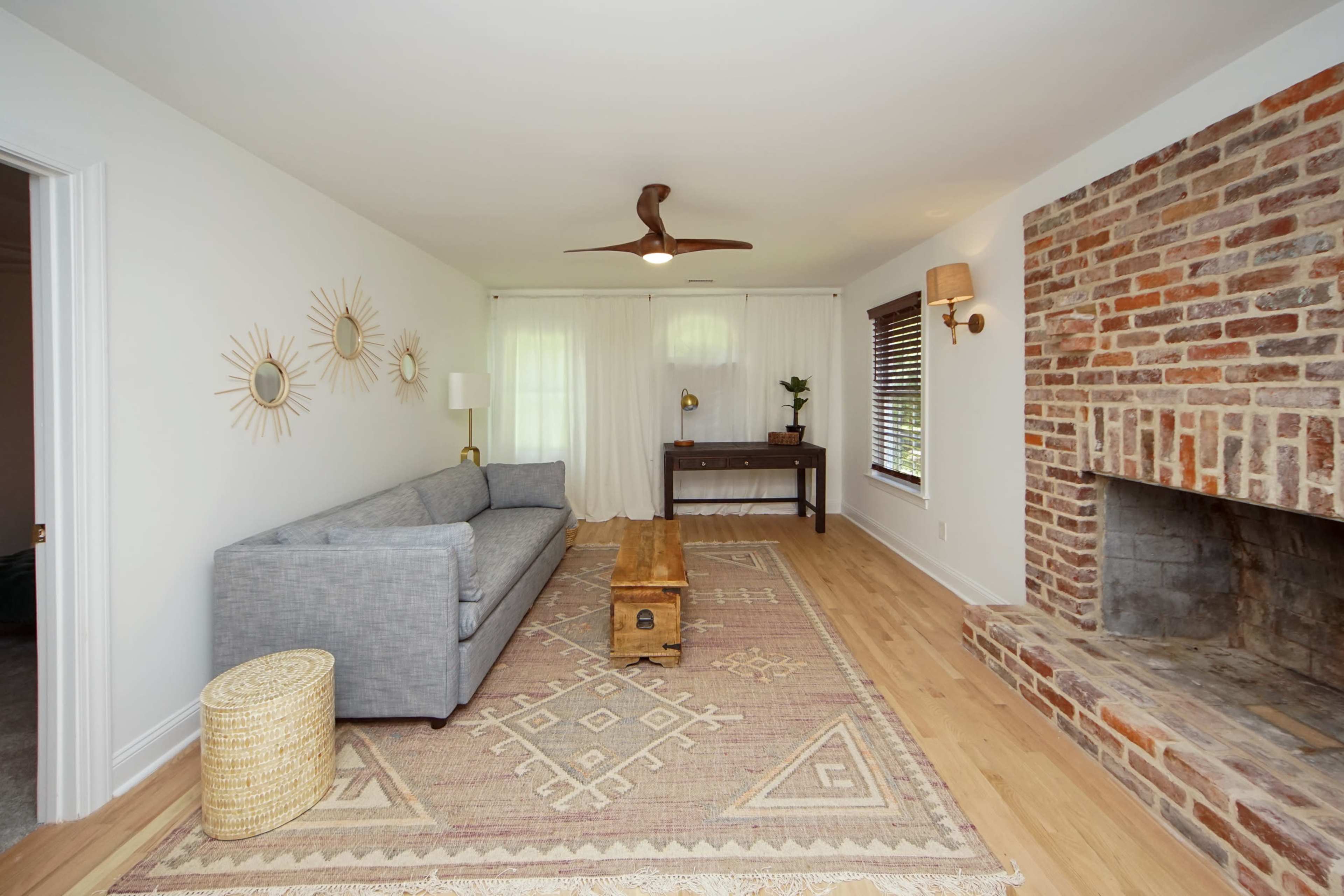 The living room features a gray sofa, a wooden coffee table, a brick fireplace, and a woven basket, all complemented by a large area rug underfoot.