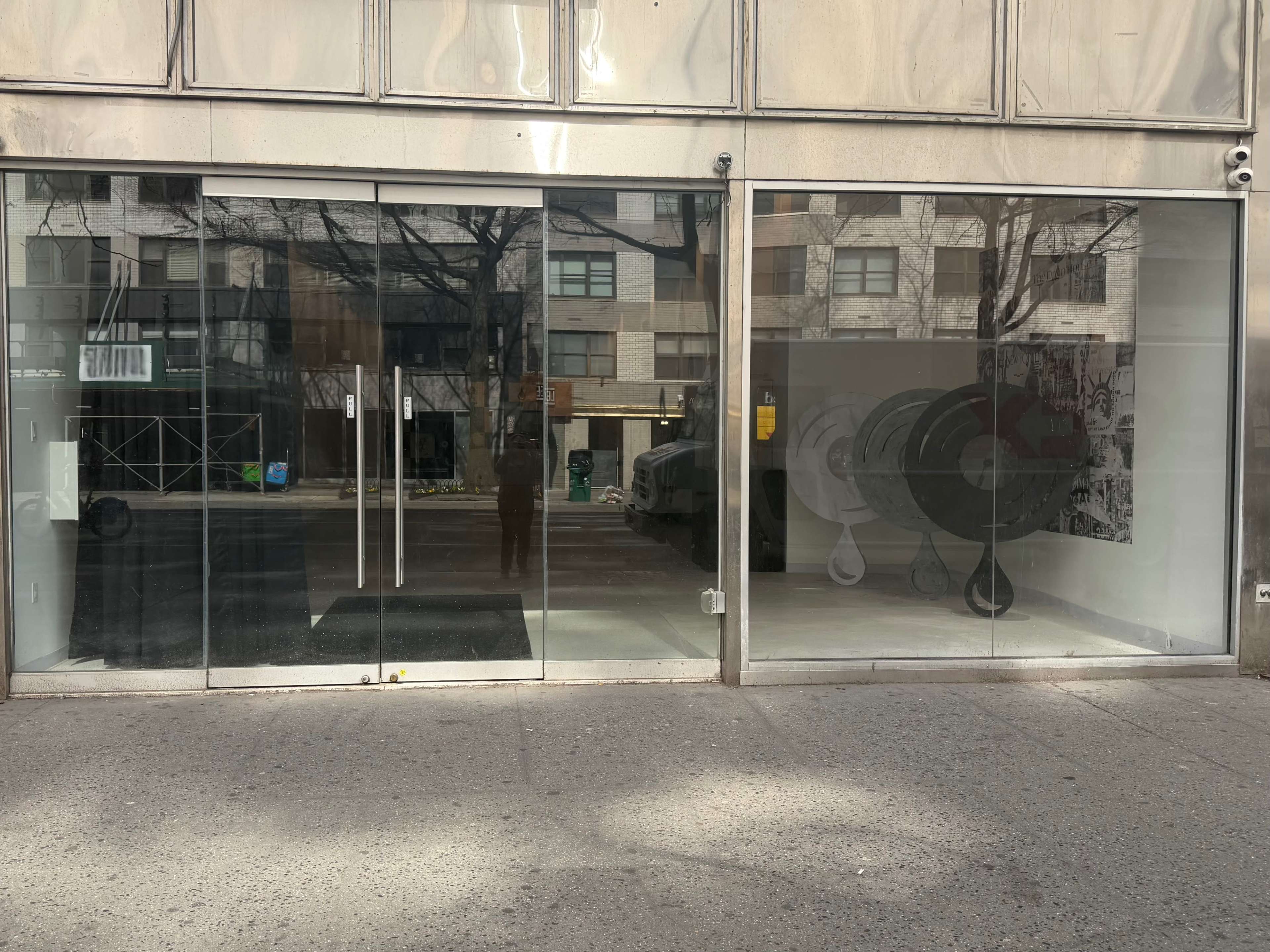 The image shows a storefront with large glass windows and a visible interior featuring a large monochromatic mural and empty space.