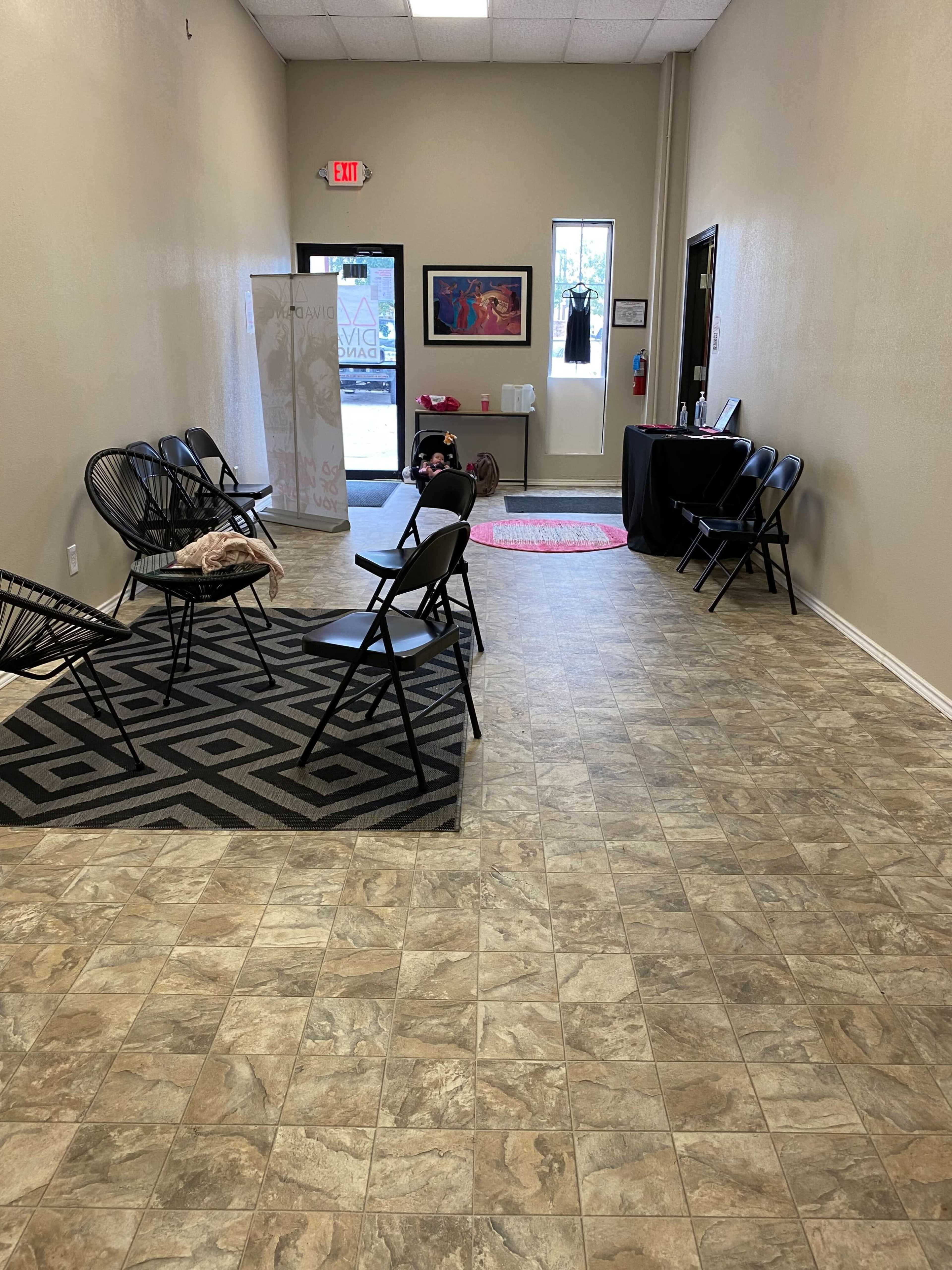 The image shows a long, narrow hallway with black chairs arranged along the sides and a reception area at the far end.