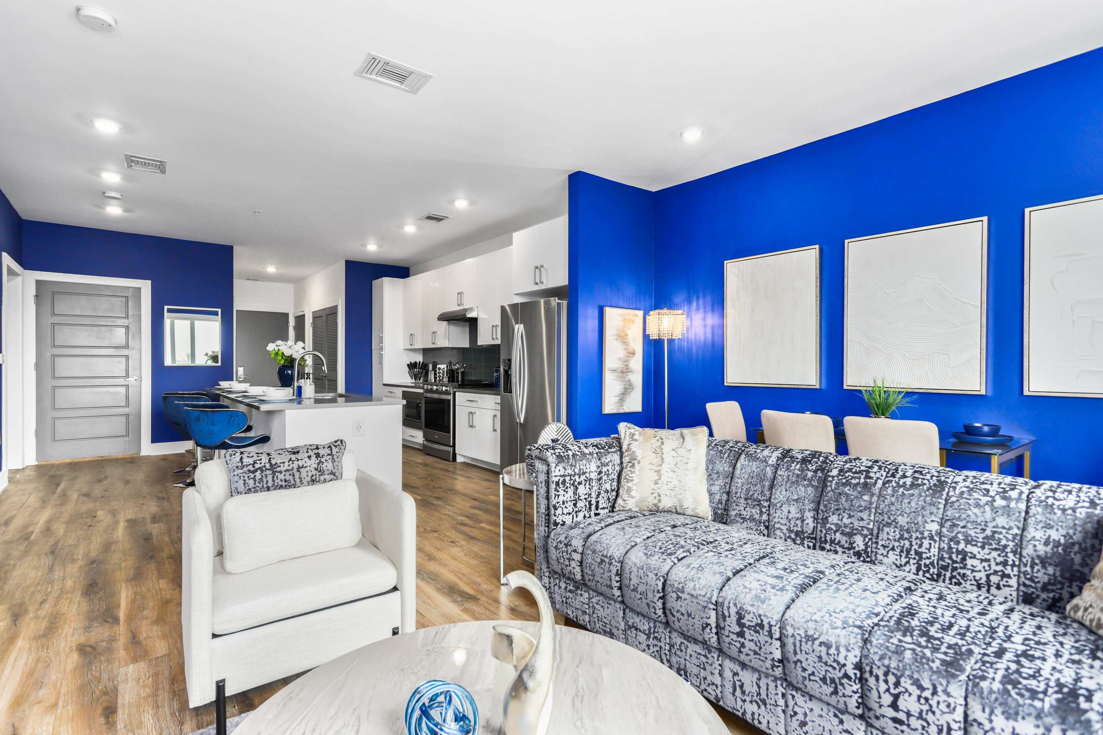 A modern living space featuring a blue accent wall, a sectional sofa, and a kitchen with stainless steel appliances.