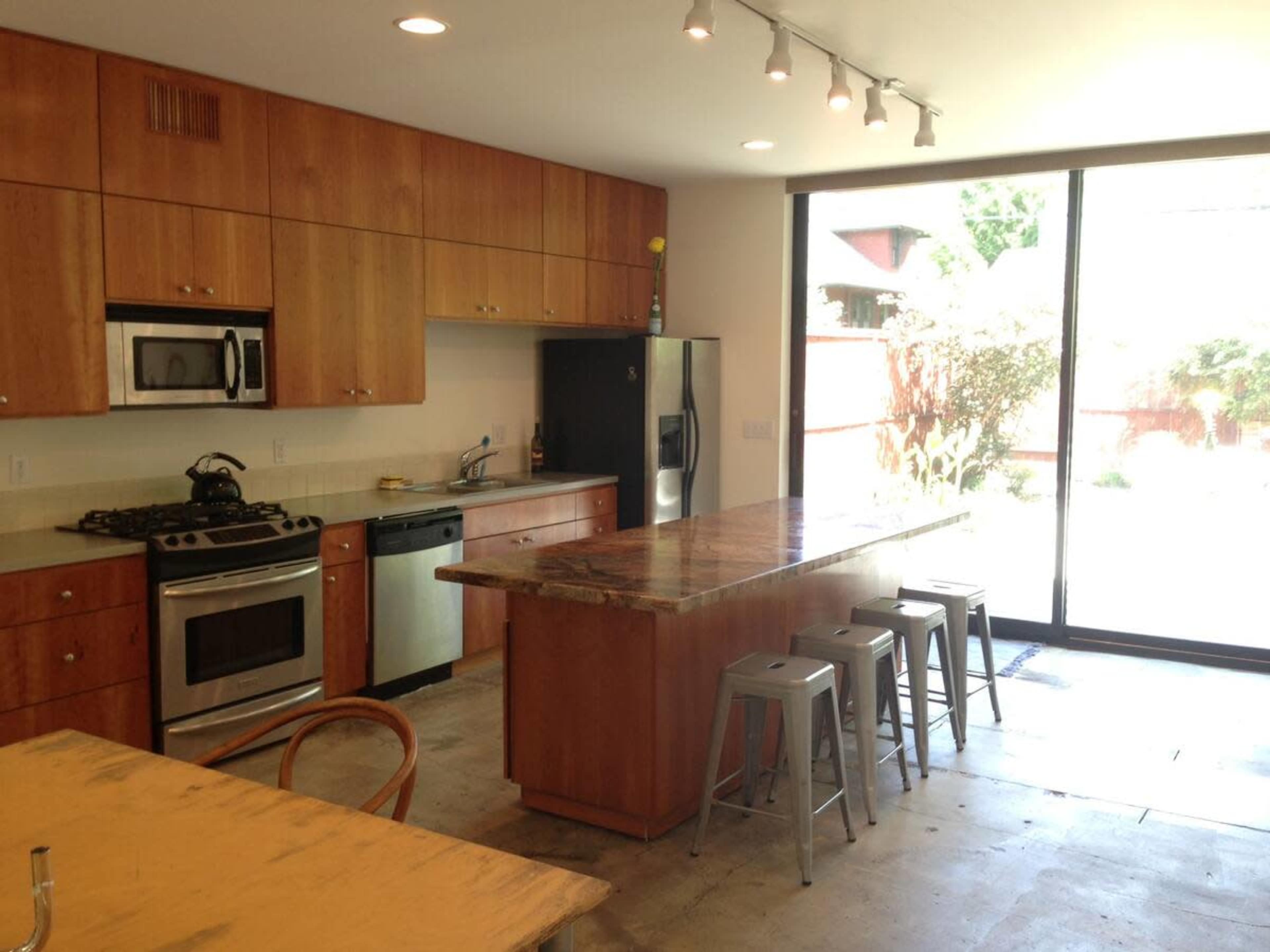 The kitchen features wooden cabinets, stainless steel appliances, a marble-topped island, and large sliding glass doors leading to an outdoor area.
