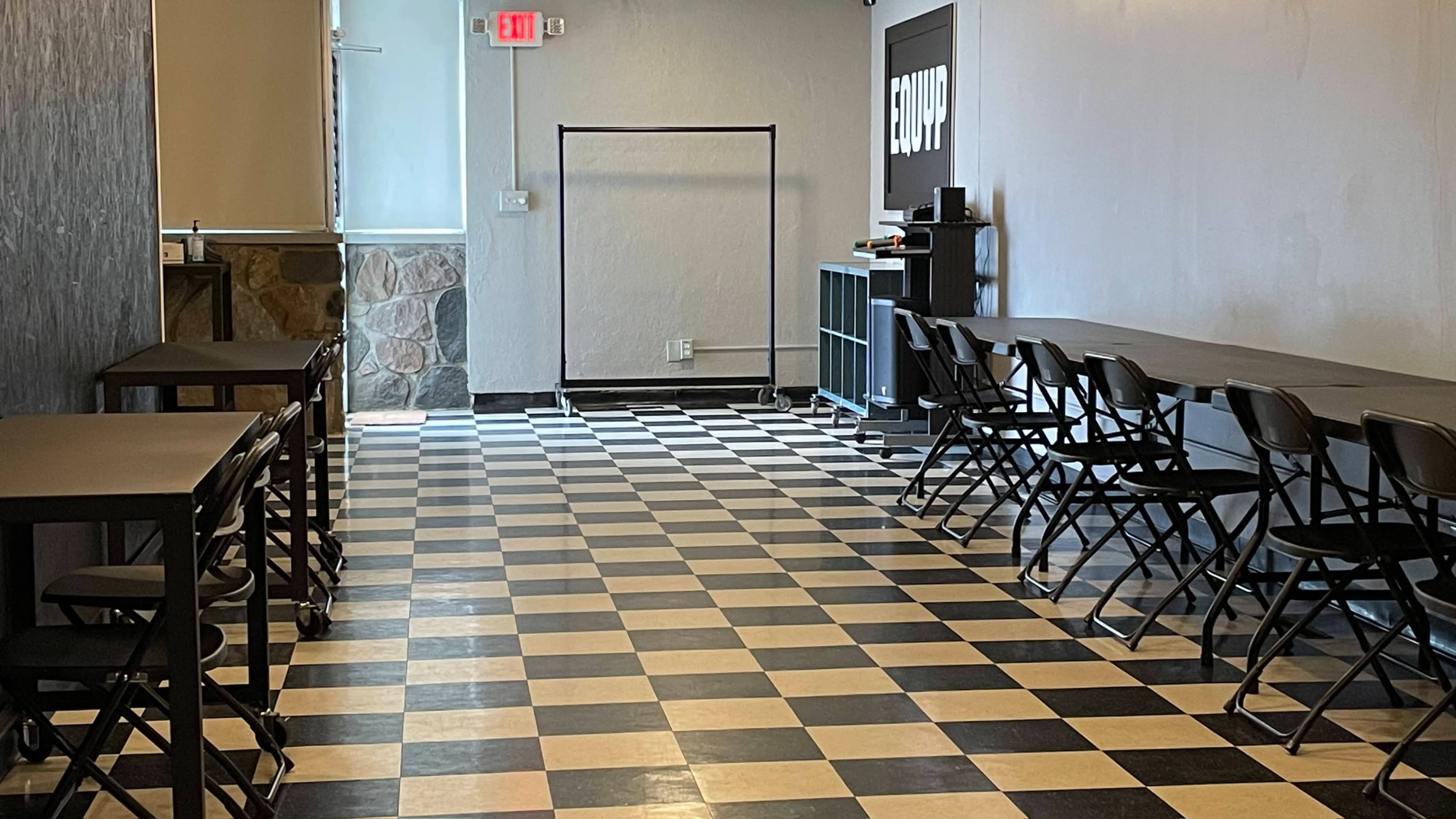 A room with black and white checkered flooring, several black folding chairs, and a table against one wall.