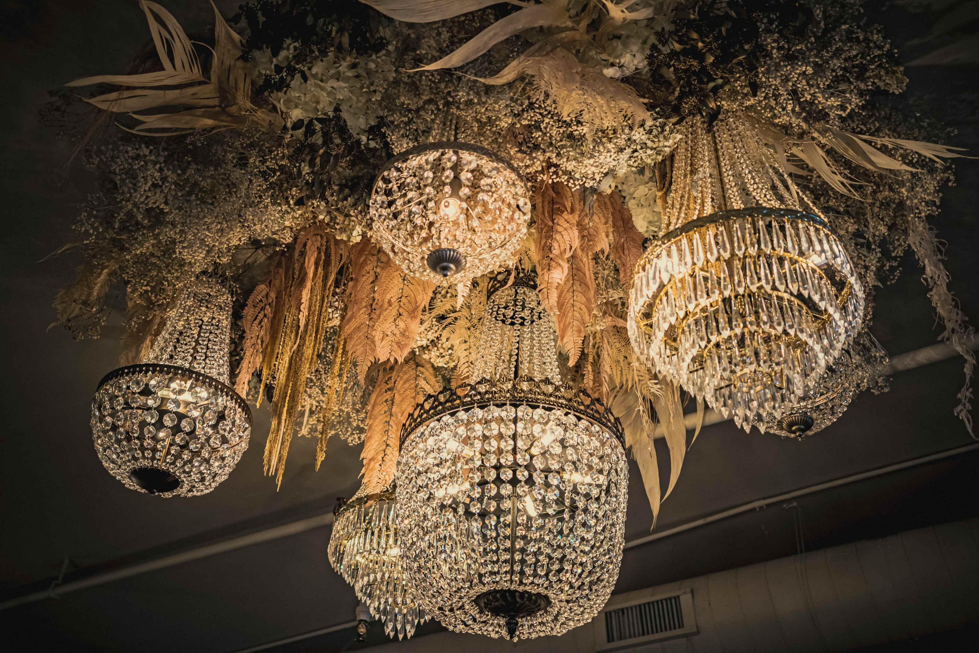 An elaborate ceiling adorned with multiple crystal chandeliers surrounded by decorative dried flowers and foliage.