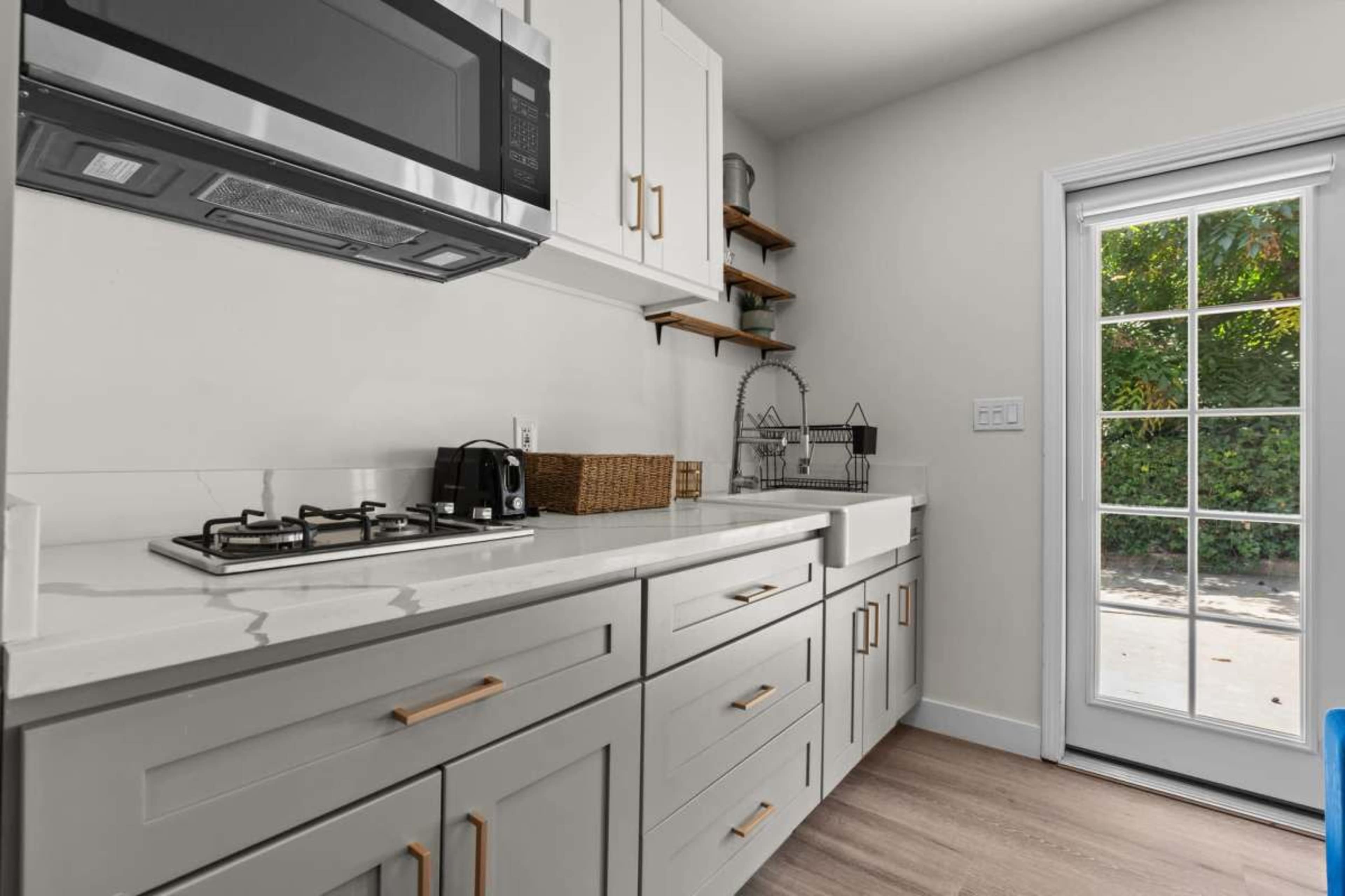The image shows a modern kitchen with white cabinetry, a microwave, a gas stove, and a large window door leading to an outdoor area.