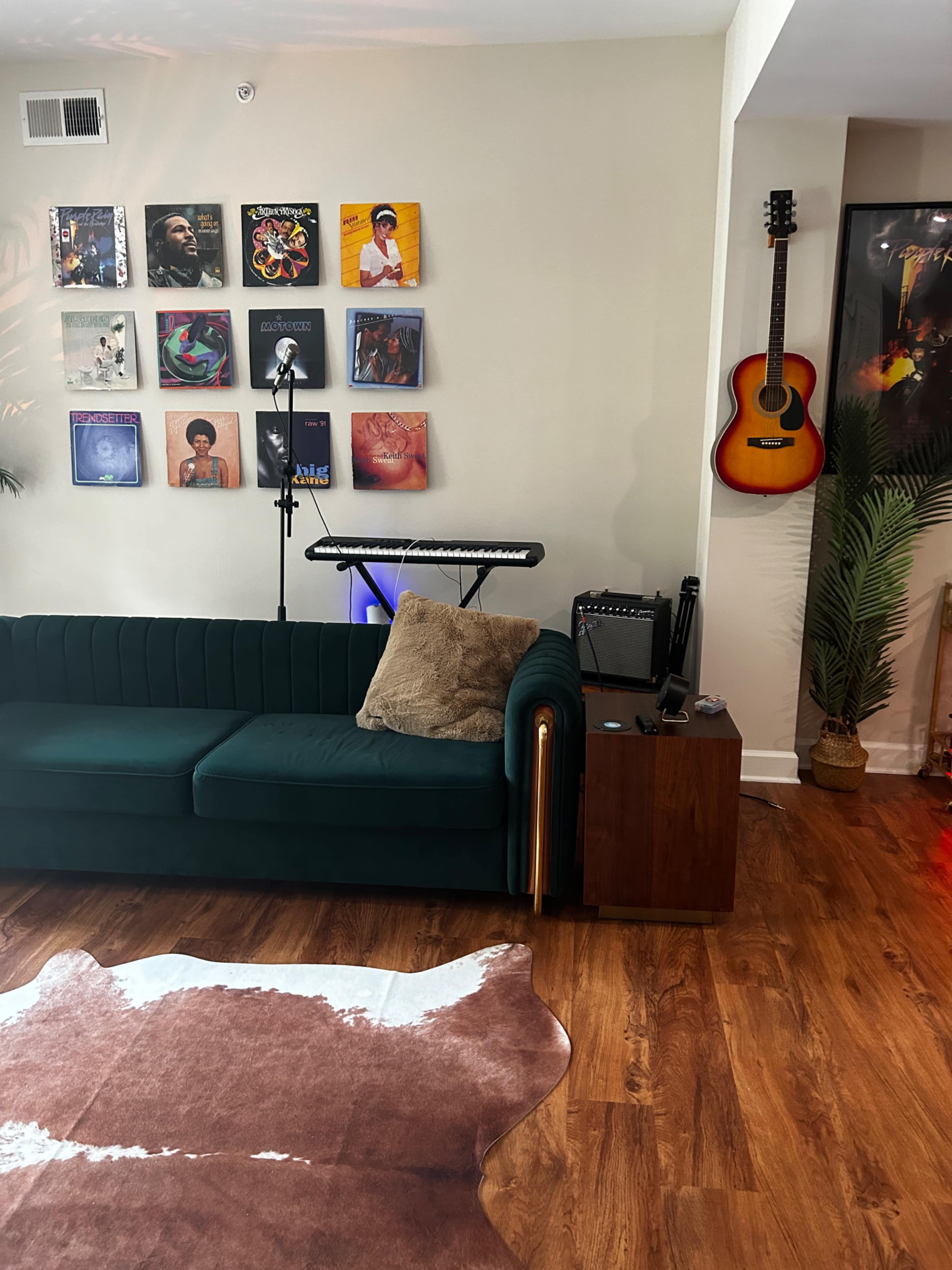 A green sofa is positioned in a room adorned with a wall of vinyl records, a keyboard on a stand, and a guitar hanging nearby.