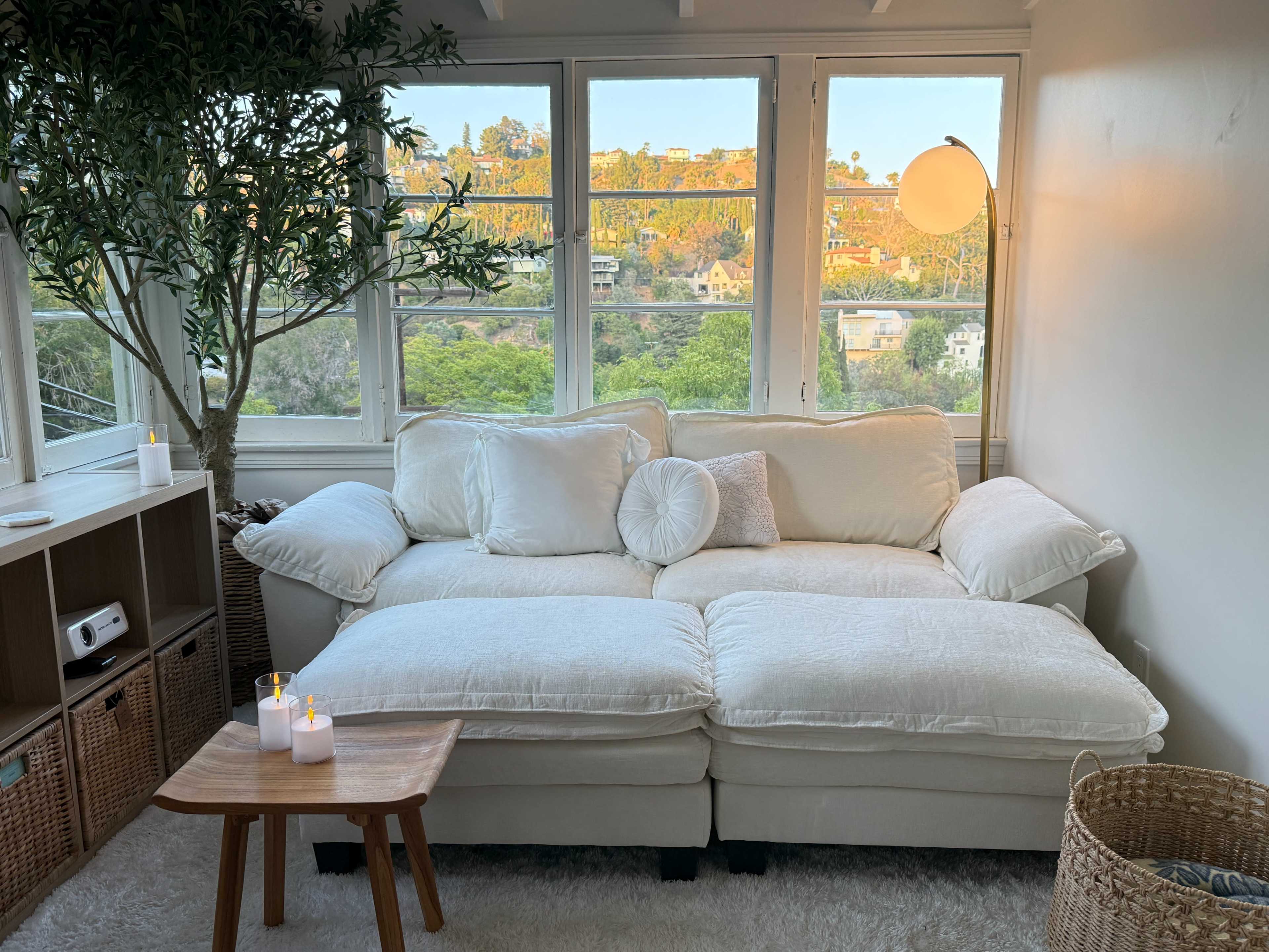 A white sectional sofa is positioned near large windows, overlooking a lush green landscape with hills in the background.