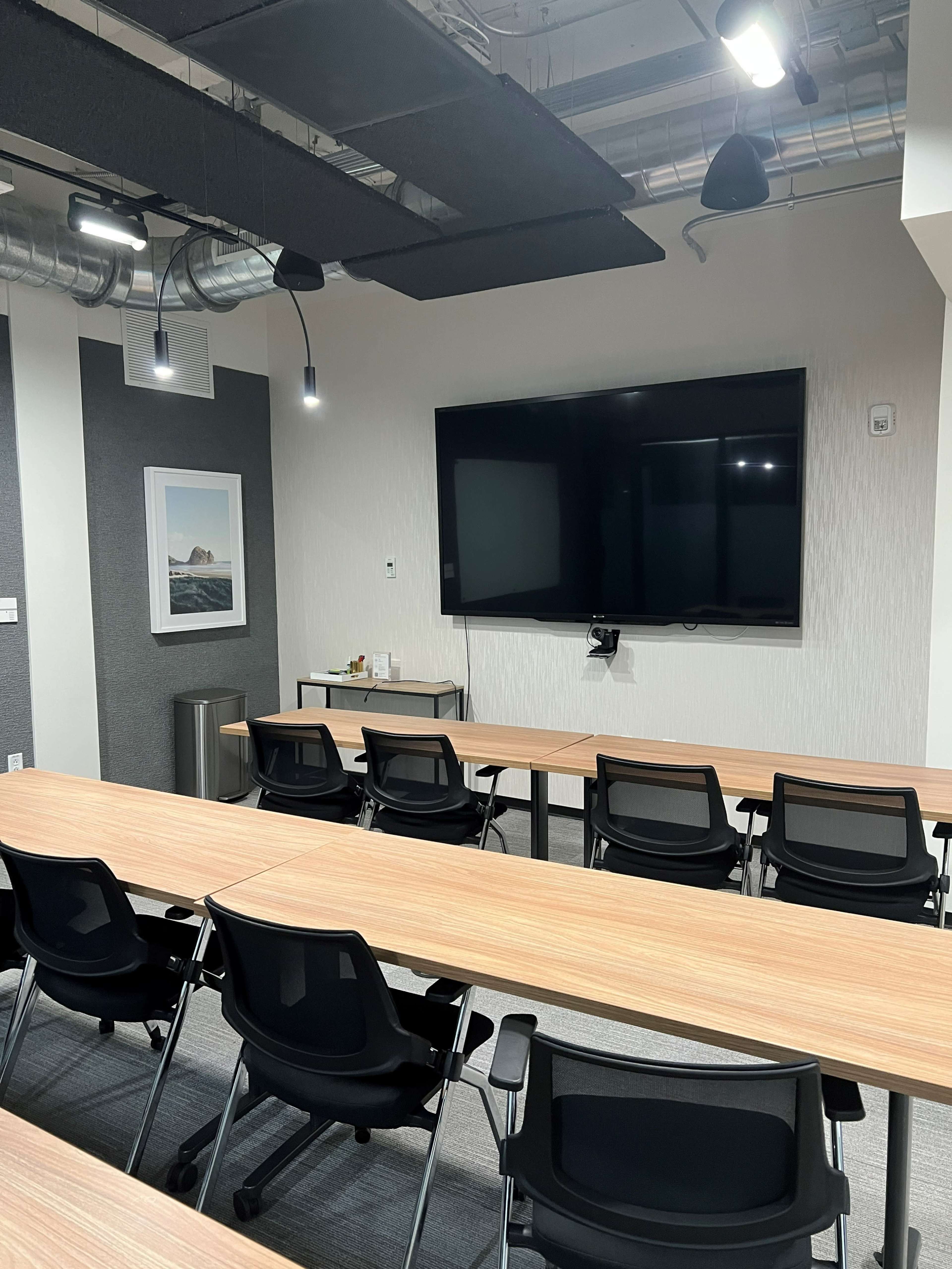 A modern conference room features a large screen, wooden tables, and black chairs arranged for meetings.