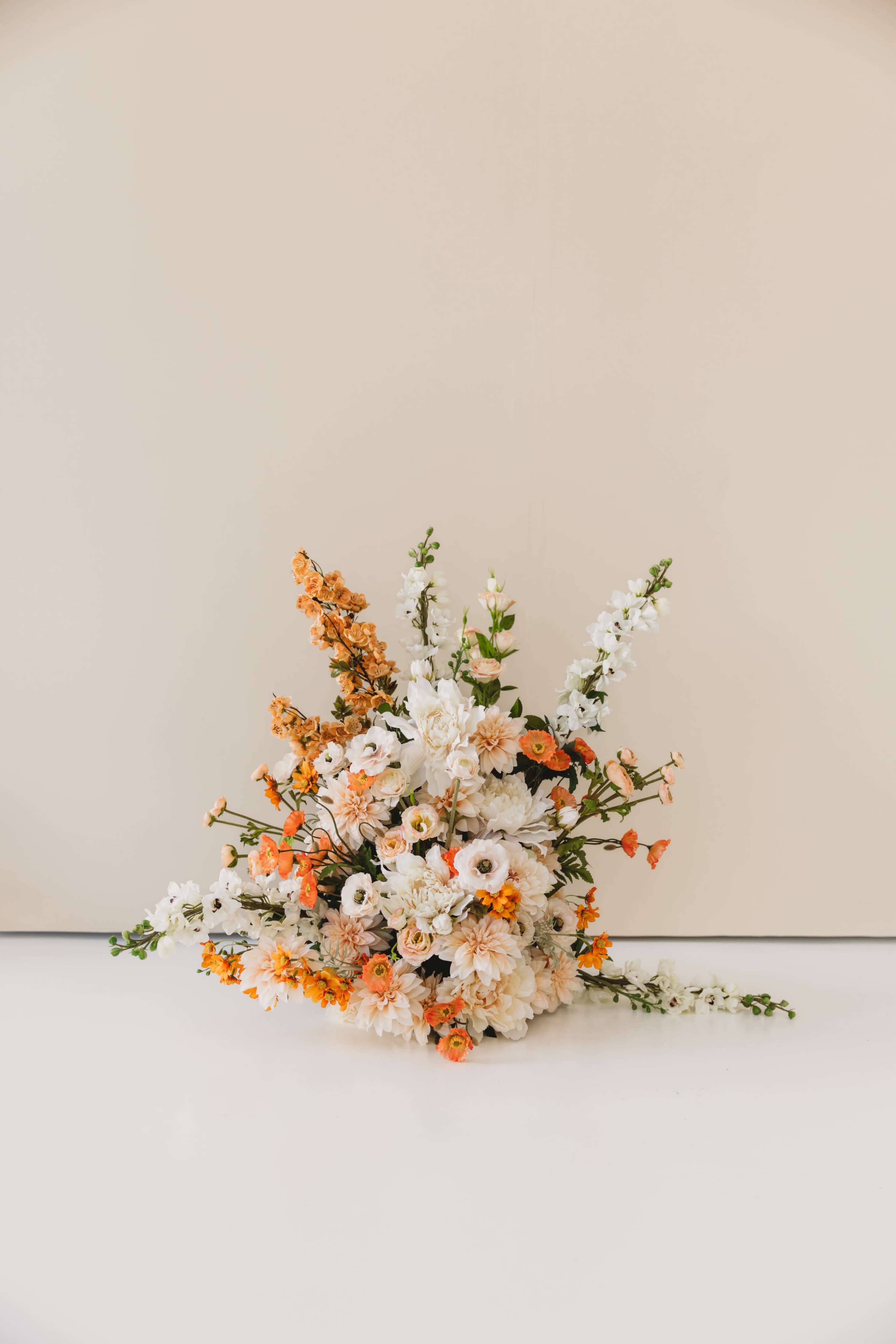 A vibrant floral arrangement featuring white, orange, and yellow flowers is displayed against a light background.