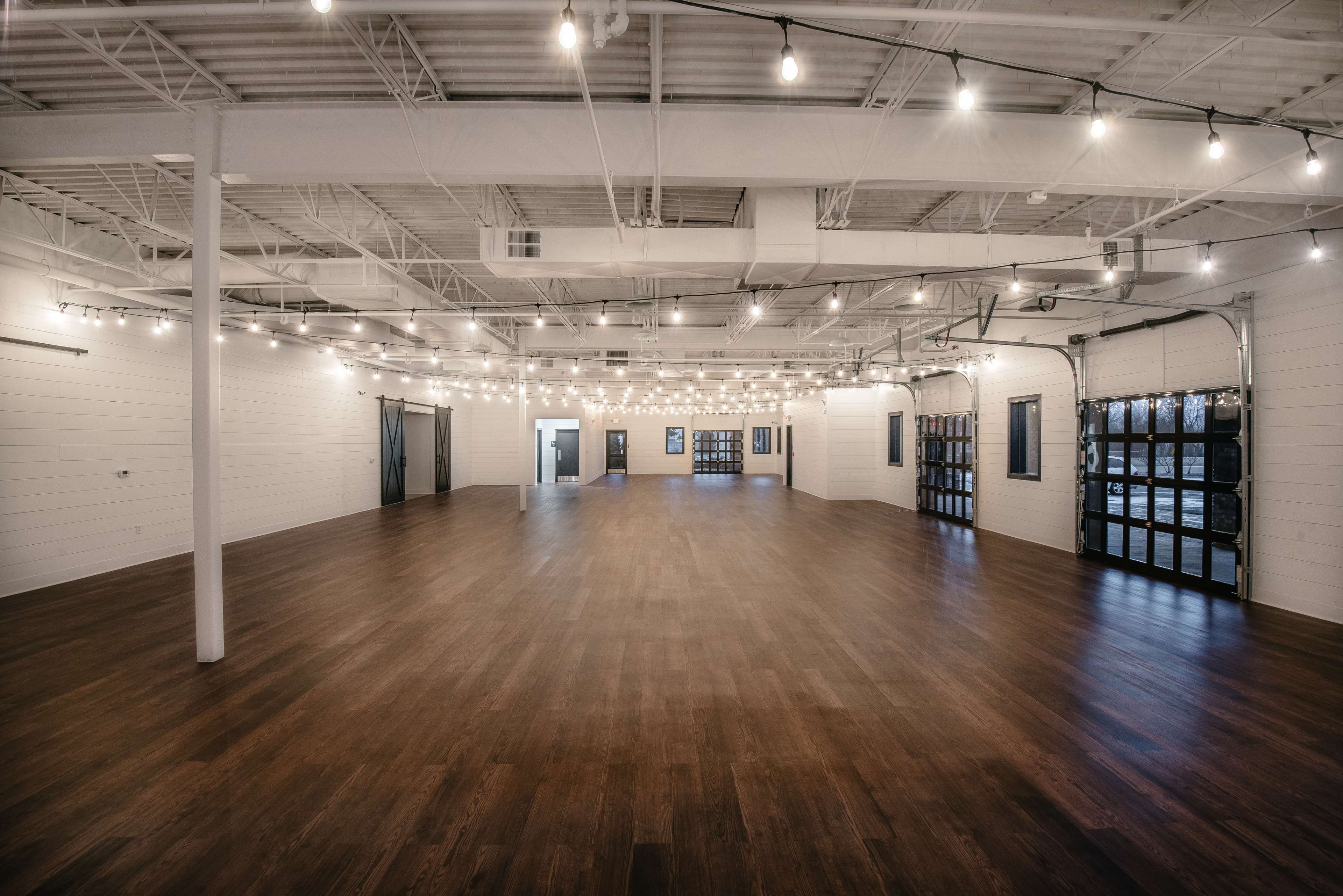 A spacious, well-lit indoor venue with polished wooden floors and string lights hanging from the ceiling.