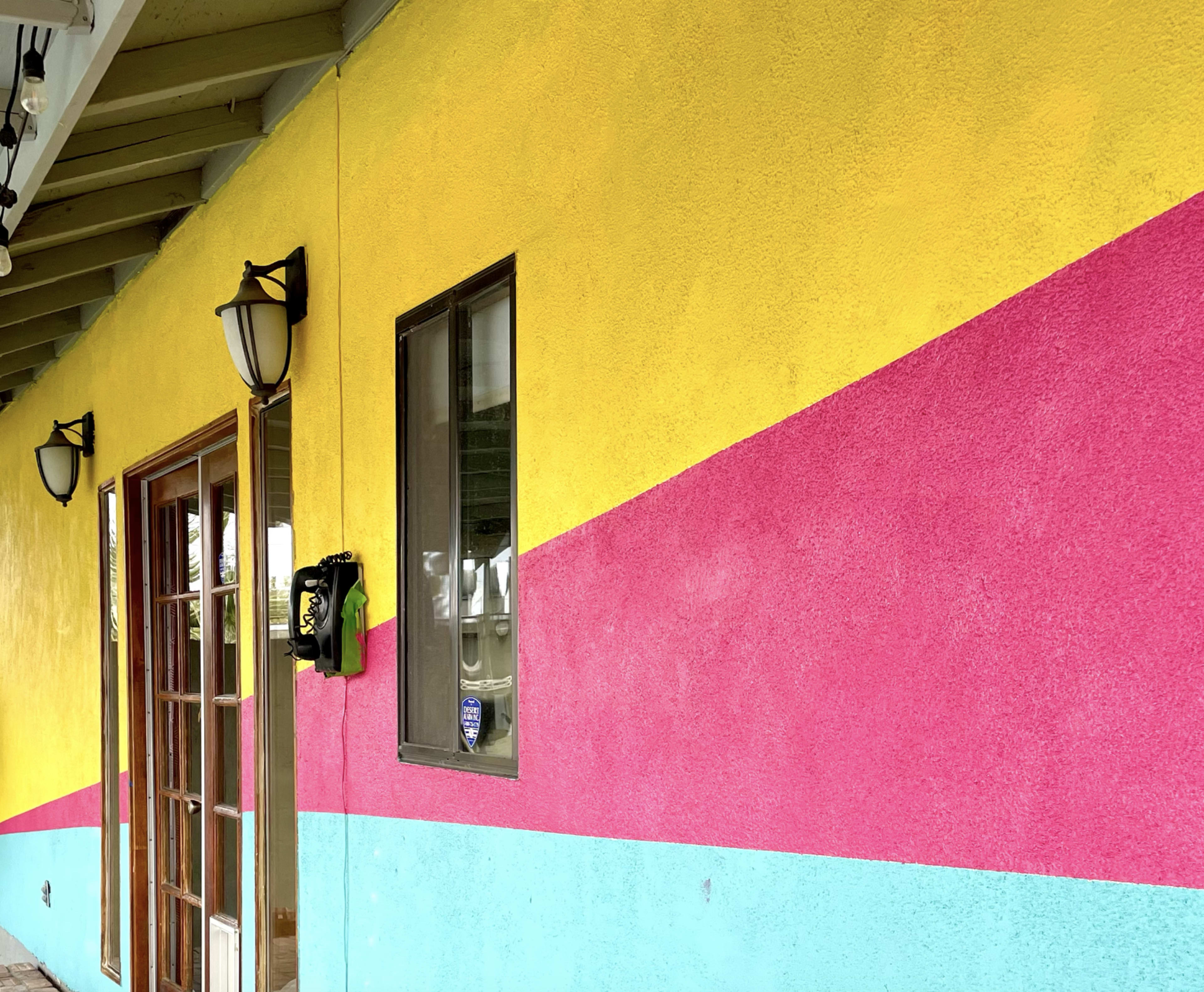 The image shows a brightly colored wall featuring yellow, pink, and aqua stripes, with a wooden door and light fixtures.