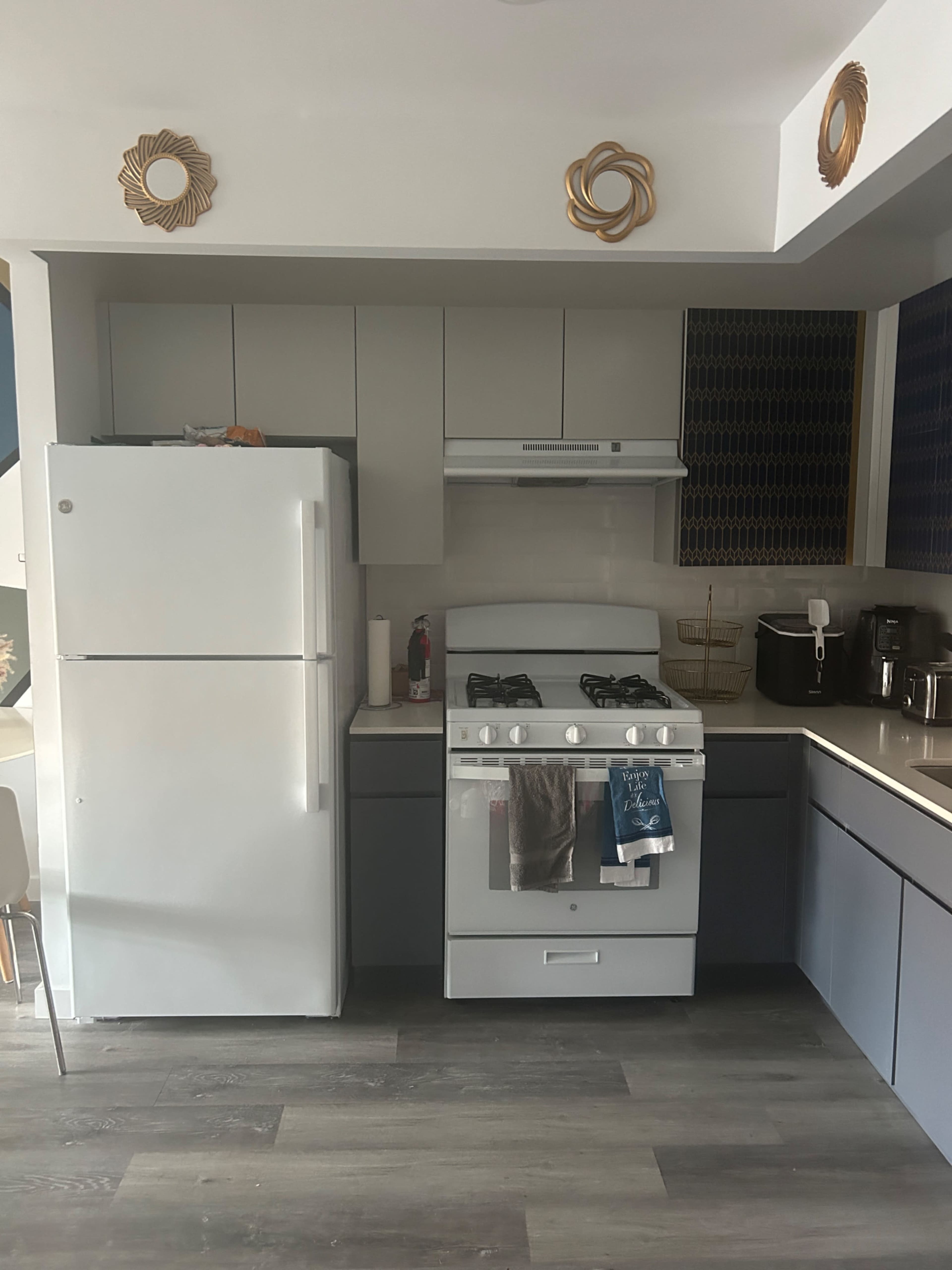 A modern kitchen features a white refrigerator, a gray oven with a stovetop, and cabinets above a countertop, with decorative elements on the walls.