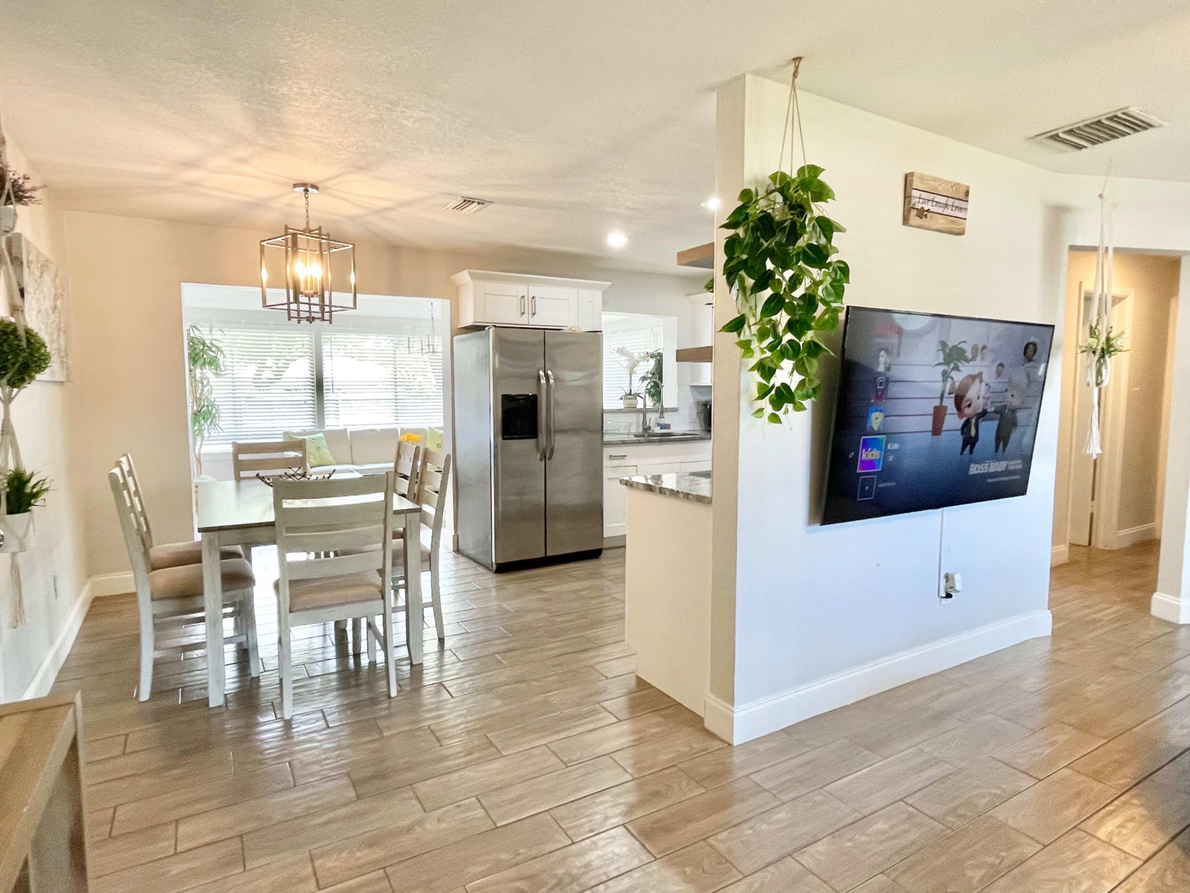 The image shows a modern kitchen and dining area with a table set for four and large windows providing natural light.
