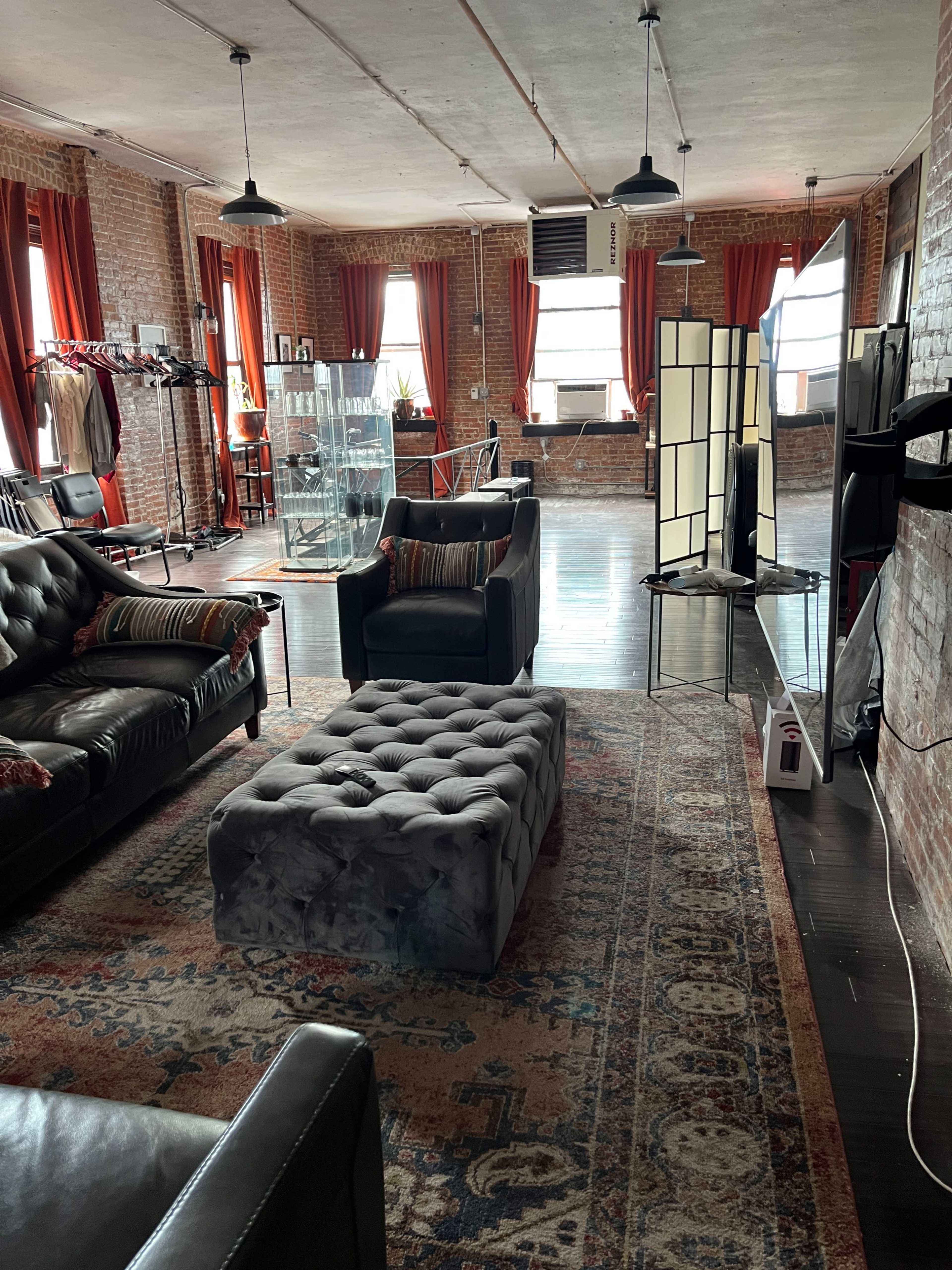 A spacious loft-style living area with exposed brick walls, large windows, and a mix of contemporary and vintage furniture.