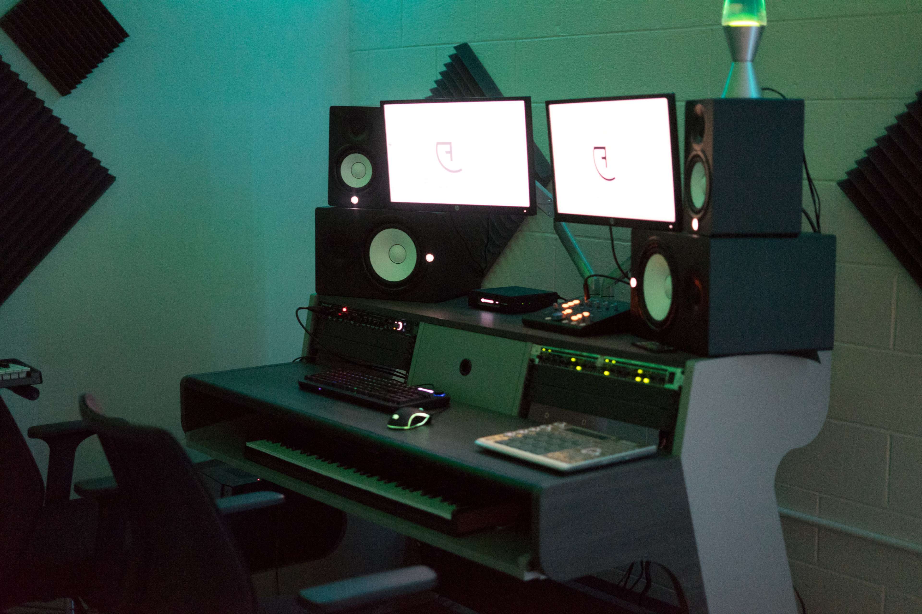 A music production studio setup with a desk, two computer monitors, speakers, and a keyboard.