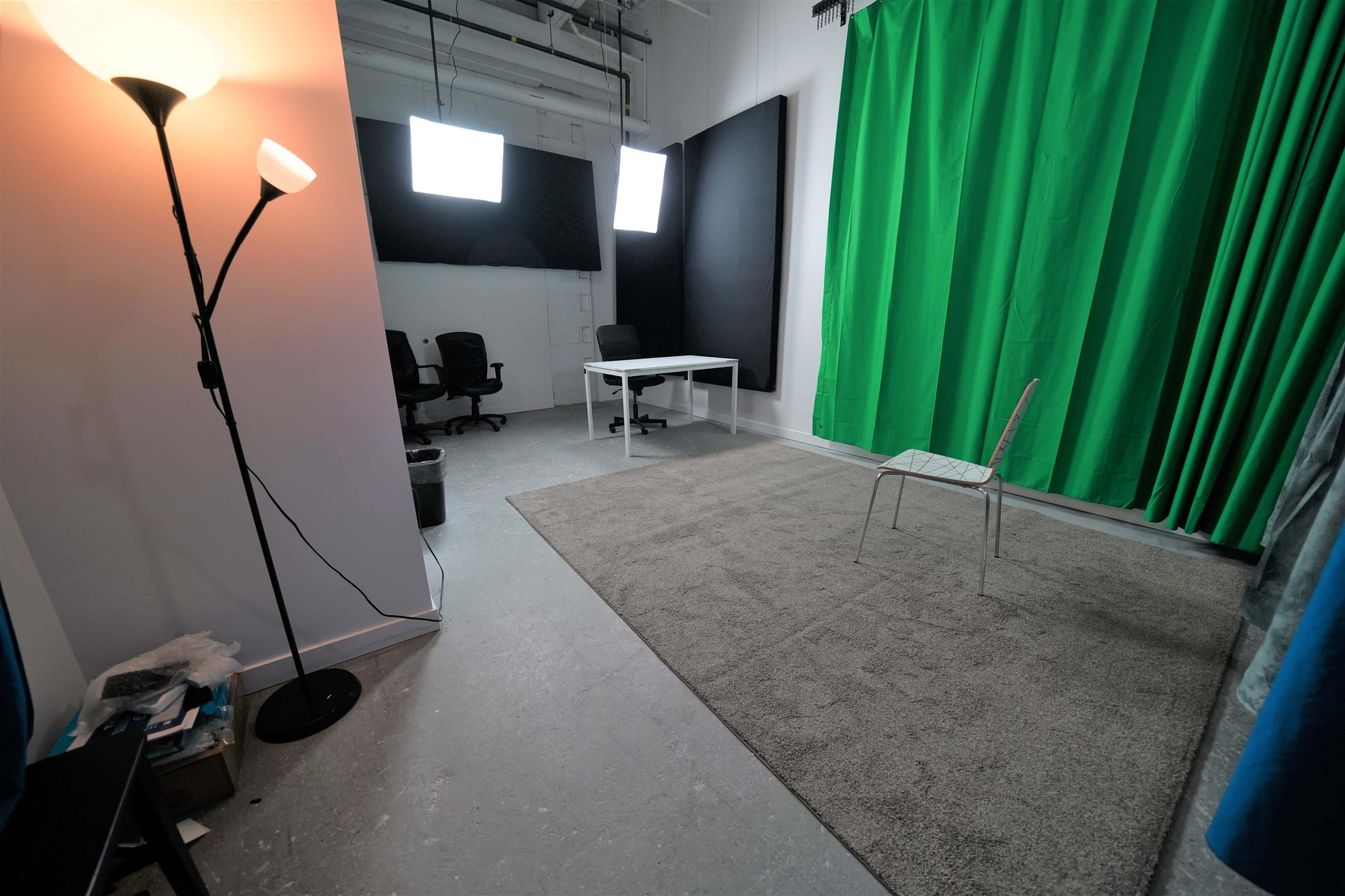 A studio space features a green backdrop, a chair, a table, and lighting equipment.
