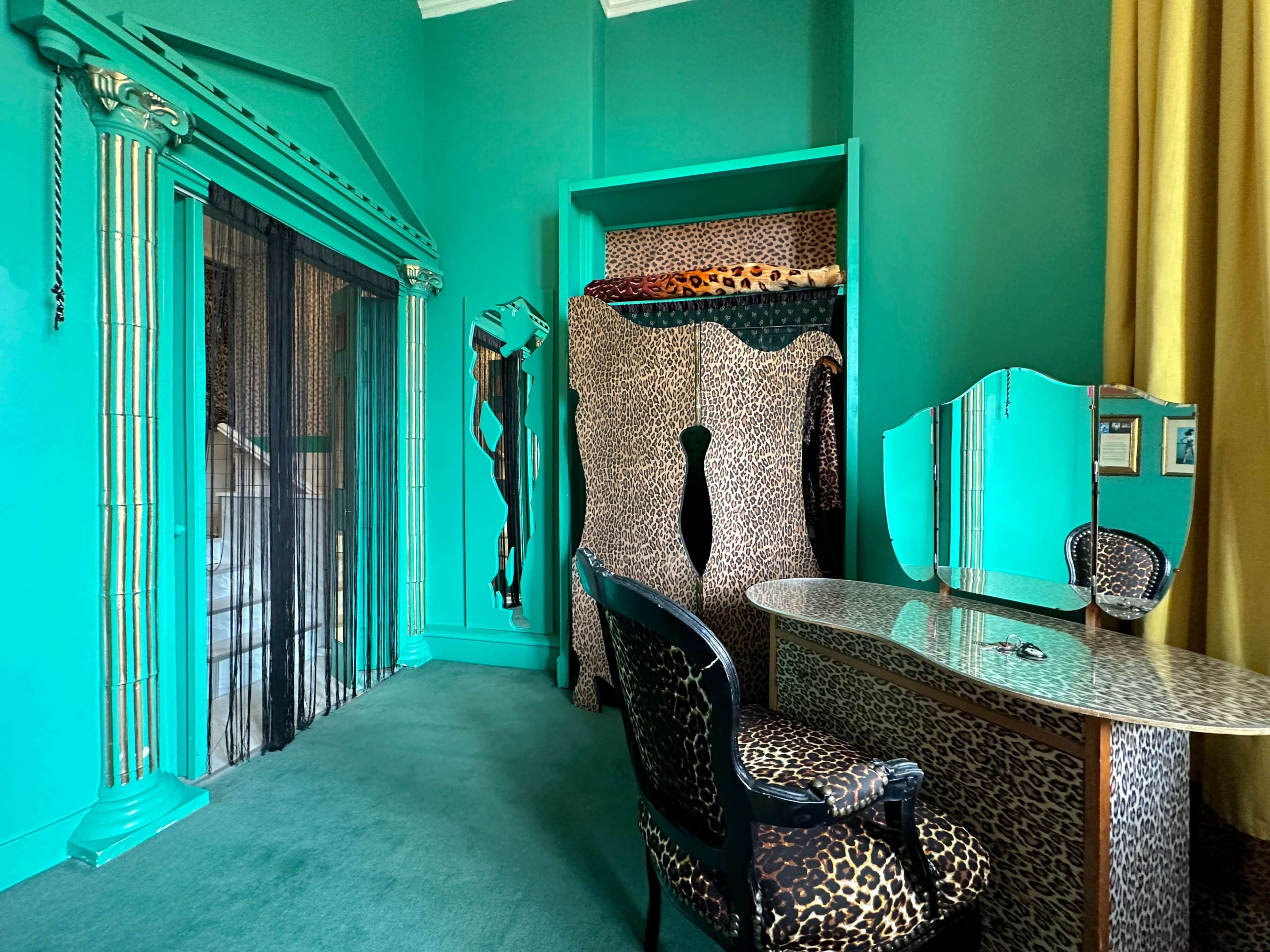 The room features green walls and leopard-print furniture, including a chair and a vanity, with a decorative mirror and a closet area.