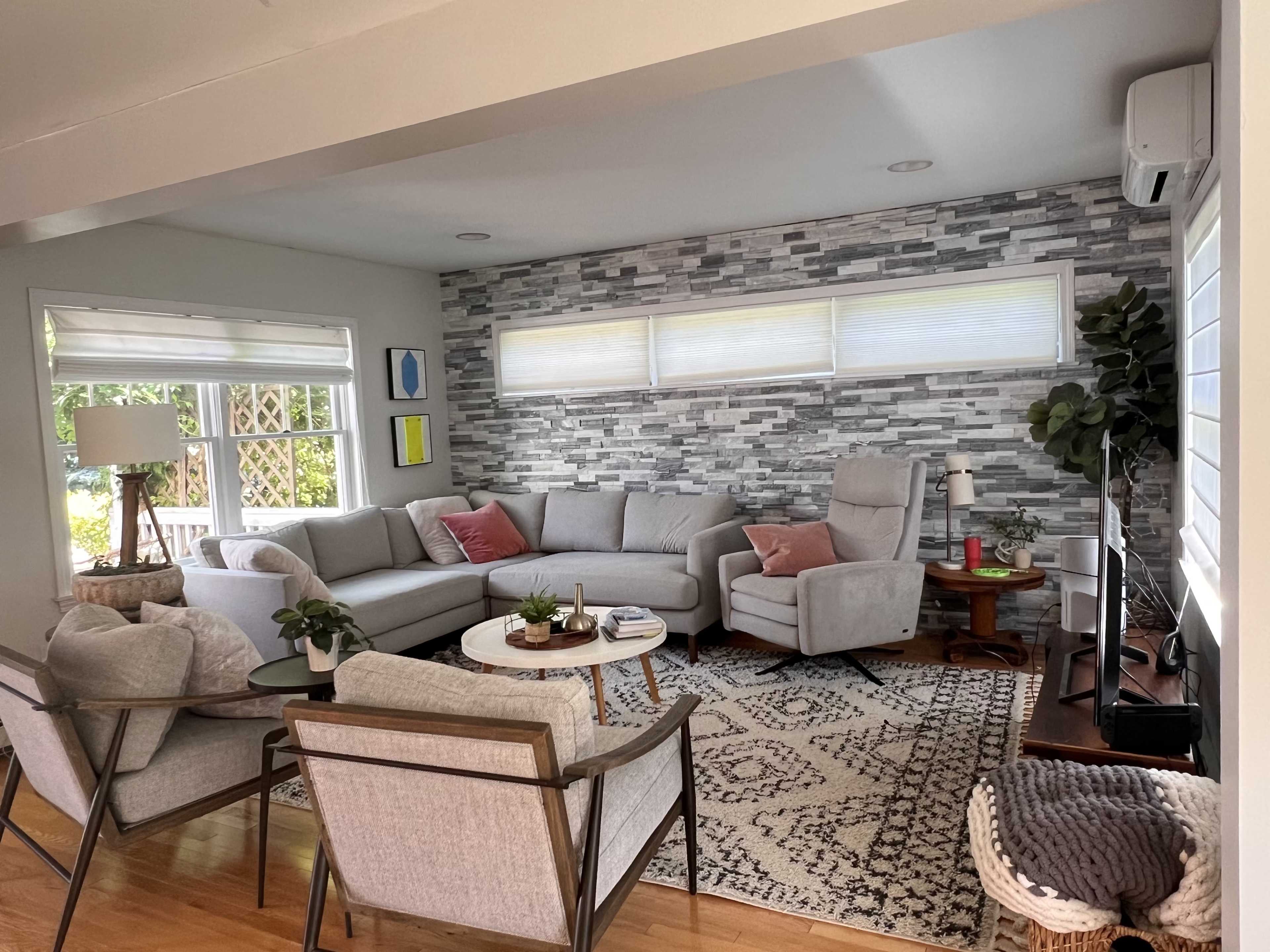 A cozy living room features a gray sectional sofa, a stylish area rug, and a wall adorned with stone panels.