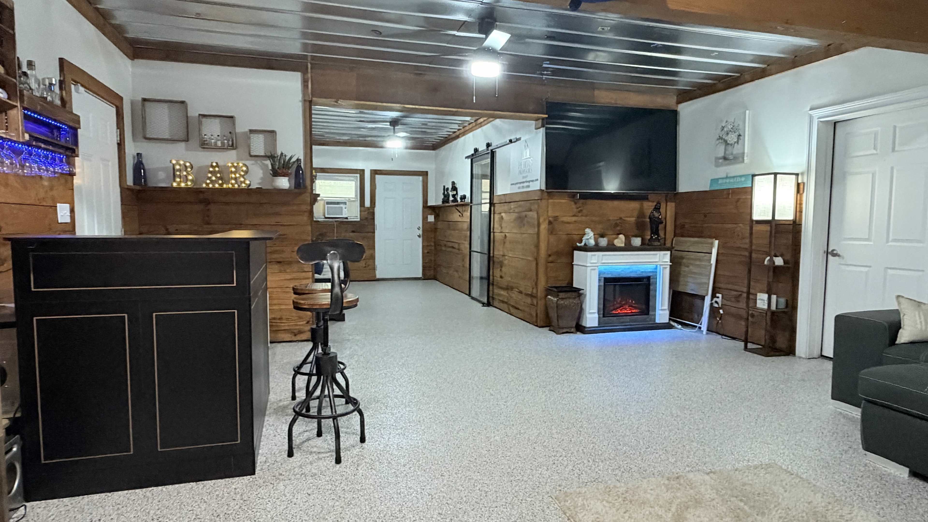 The image shows a modern interior space featuring a bar area, a fireplace, and a cozy seating arrangement, all set against wooden walls and a glossy floor.