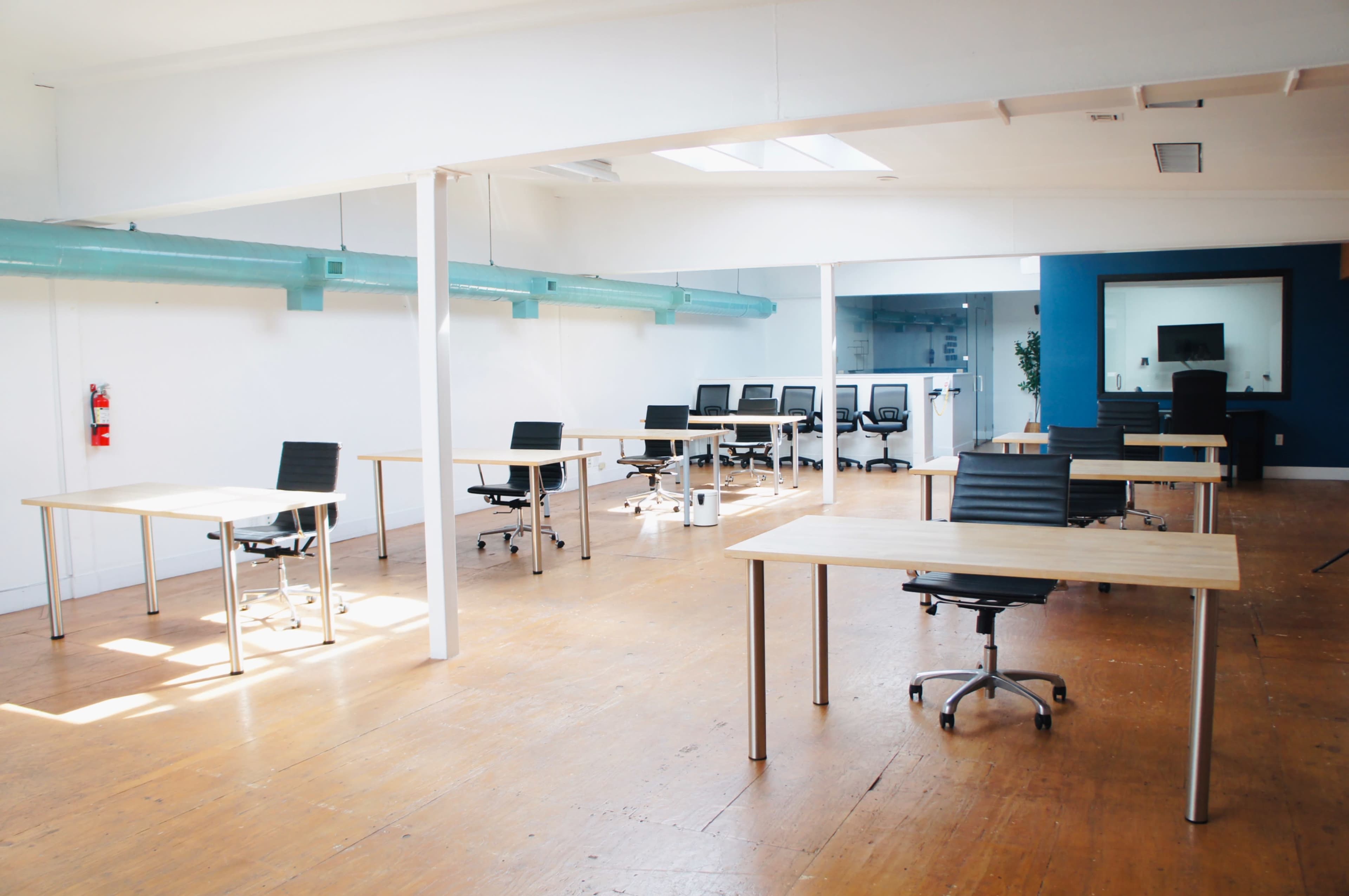 The image shows an empty office space with several desks and chairs arranged in a spacious layout.