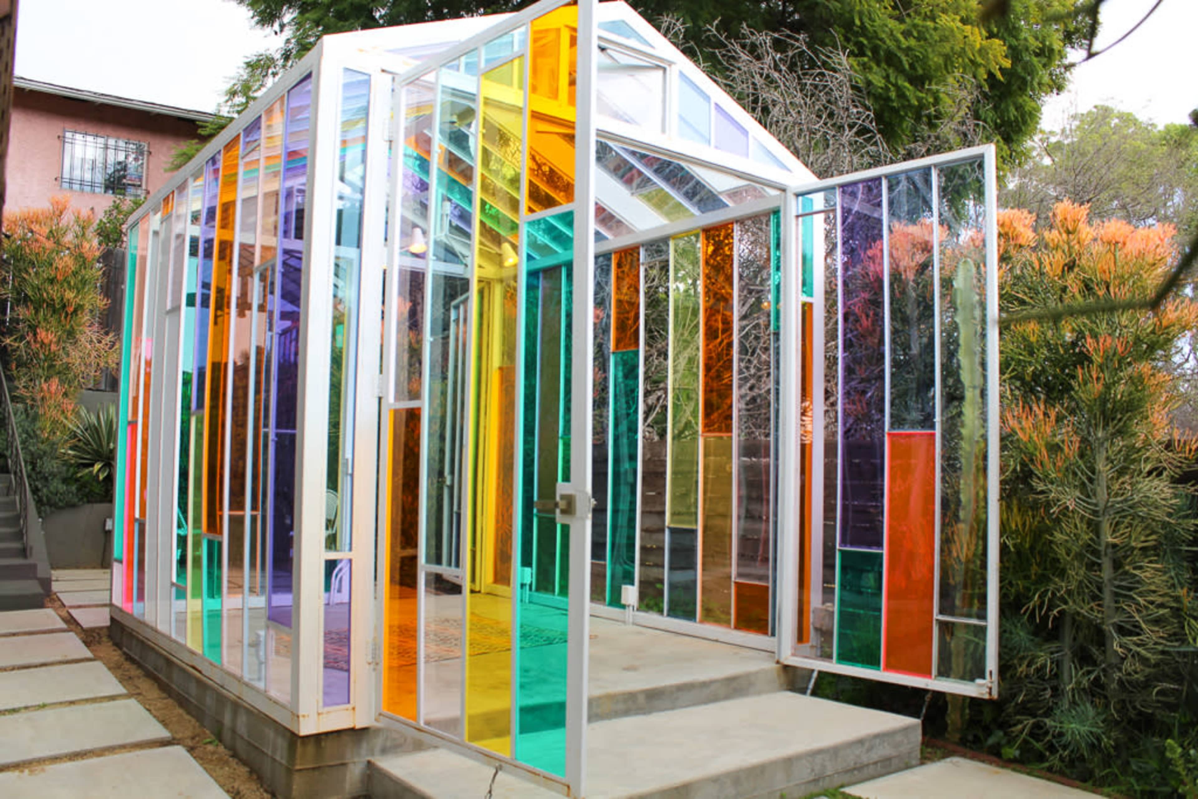 The image shows a colorful glass greenhouse surrounded by plants and flowers.