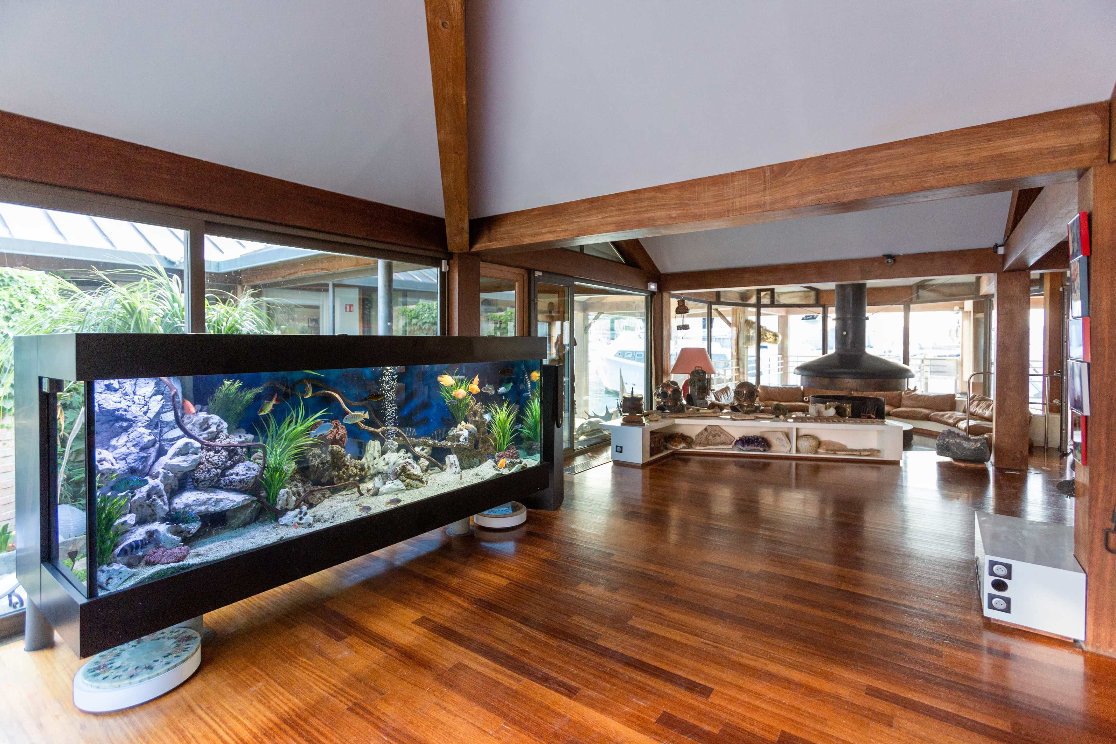The image shows a spacious living area featuring a large aquarium on the left and a modern fireplace with a wooden structure in the center.