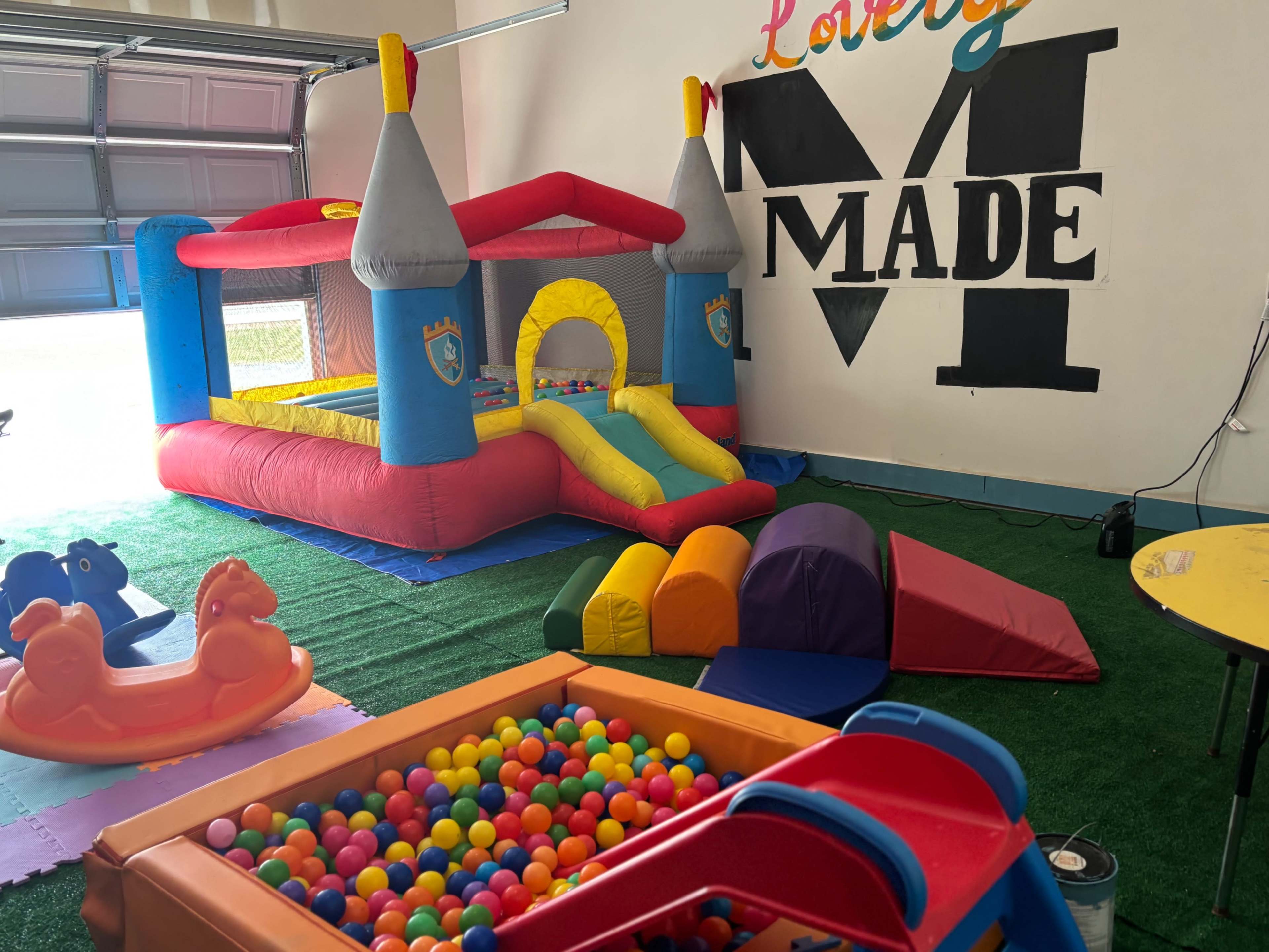 The image shows a colorful indoor play area featuring a bounce house, soft play equipment, and a ball pit.