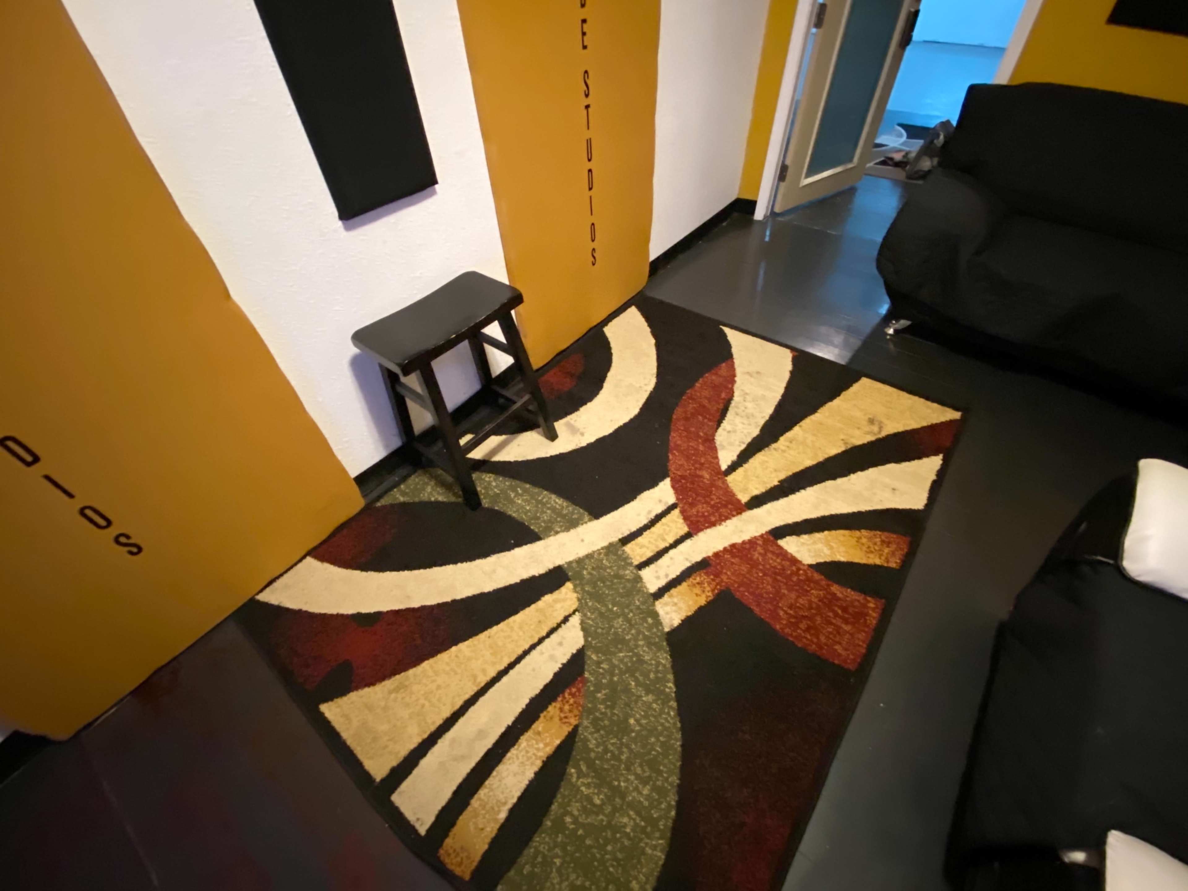 A corner of a room featuring a patterned rug, a black stool, and walls painted in yellow with black accents.