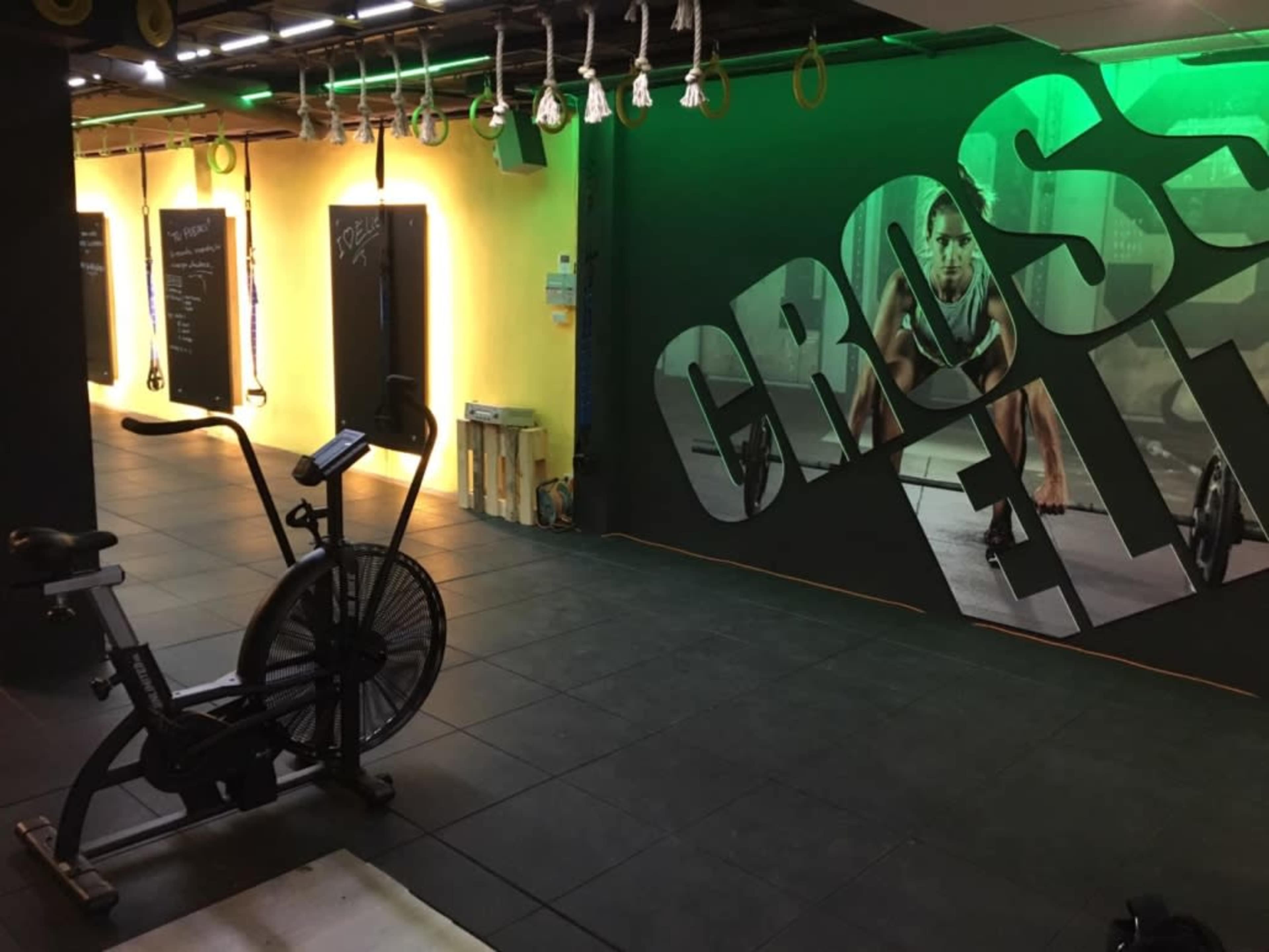 A fitness studio with an exercise bike in the foreground and a large wall mural of a person working out in the background, illuminated by green and yellow lighting.