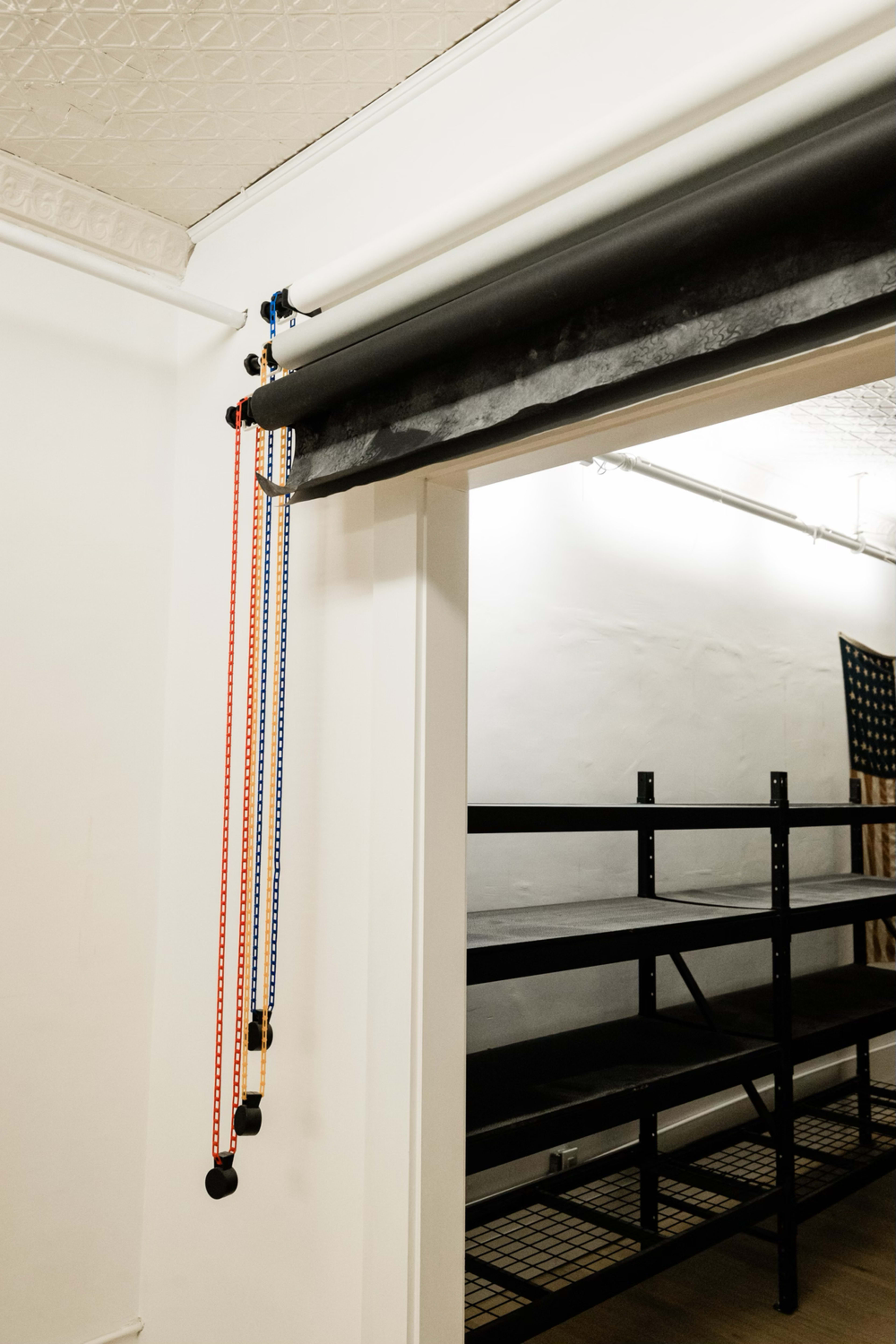 A set of color-coded ropes is attached to a mounted roller system in an empty room with black shelving.